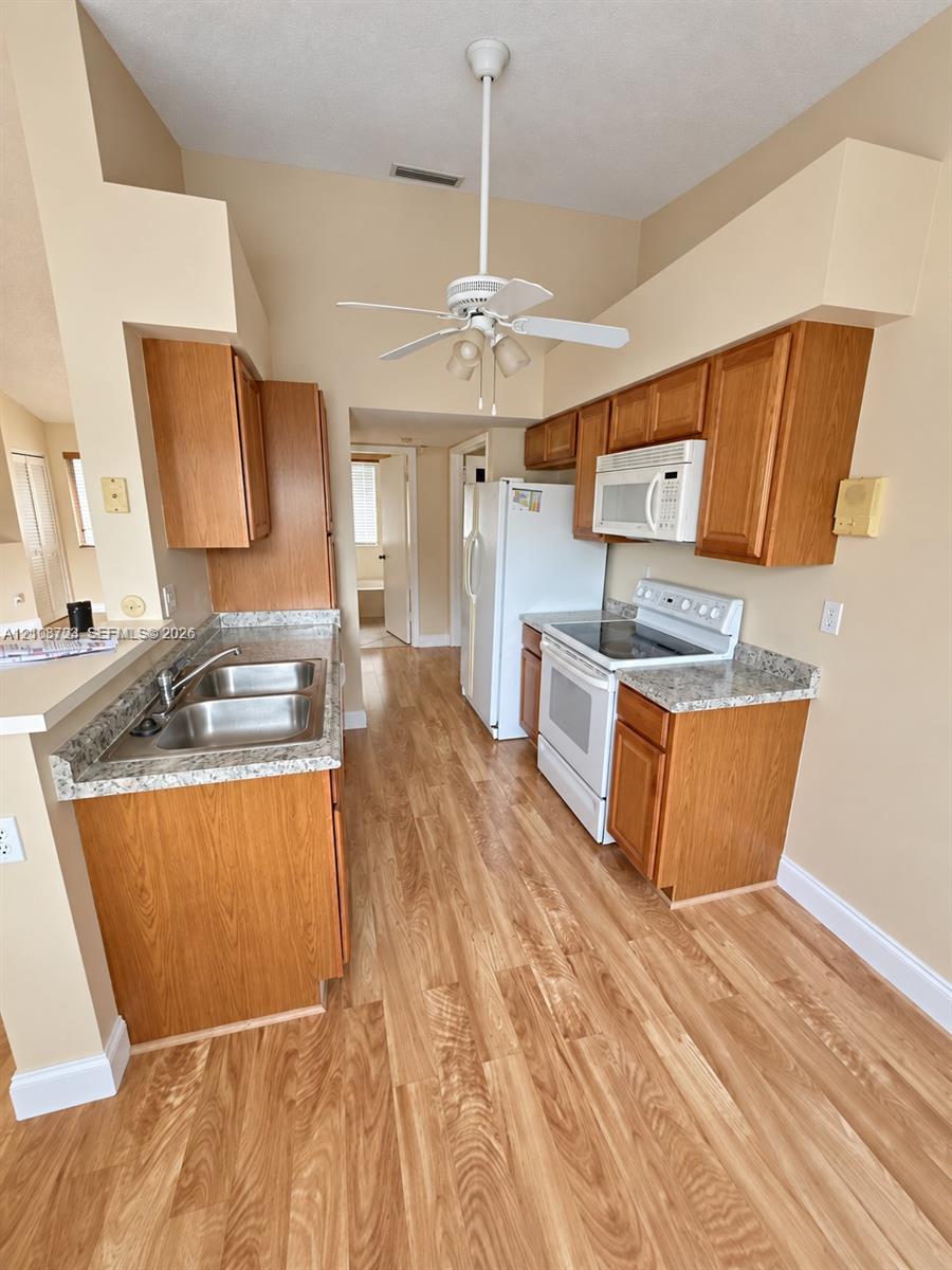 Kitchen featuring wood-finish cabinetry, stone-style countertops, stainless steel dual-basin sink, wood-finish flooring, and ceiling-mounted light fixture with fan