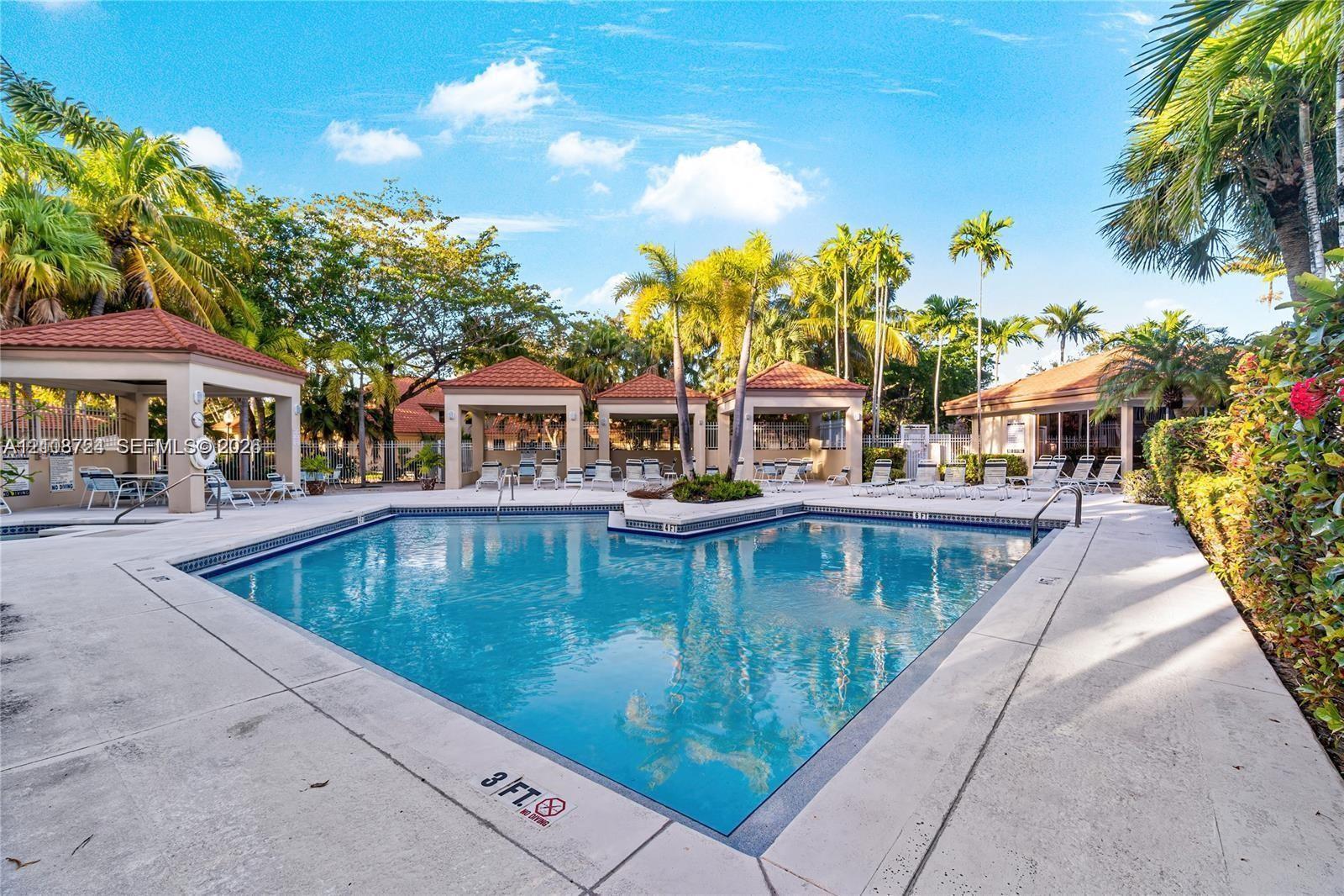 Swimming pool area with concrete decking, tile-roofed cabanas, and established palm trees
