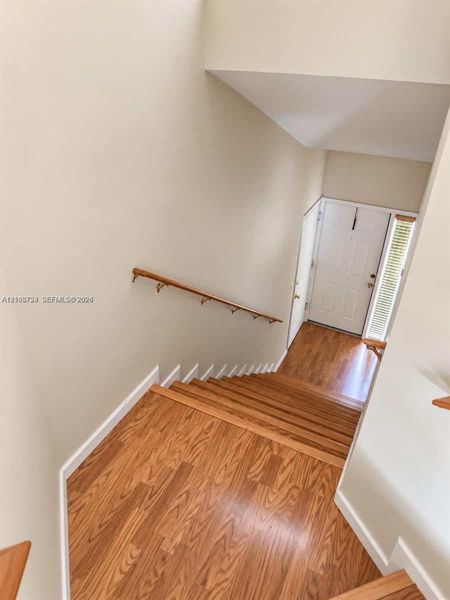 Staircase featuring wood-finish flooring, a wall-mounted wooden handrail, and an entry door with a side window panel