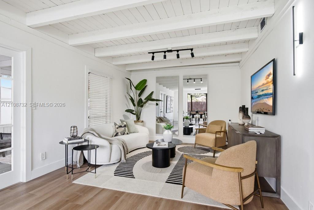 Exposed beam ceiling with white finish, wood-finish flooring, adjustable track lighting, and wall-mounted linear light fixtures