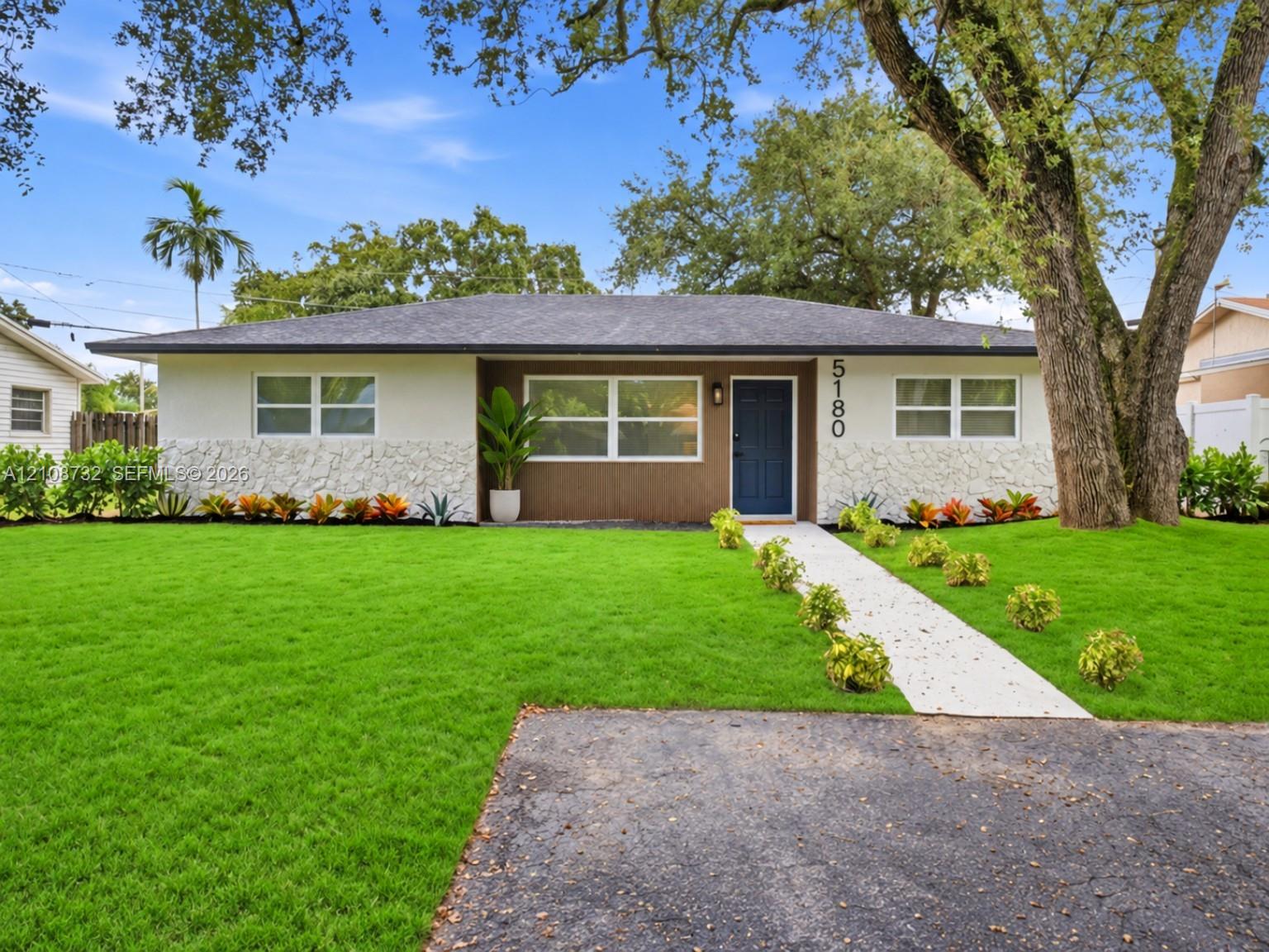 Single-story exterior featuring light-toned textured stone accents, a deep-toned shingled roof, a central entry with a paneled door, and a concrete walkway Single-story exterior featuring light-toned textured stone accents, a deep-toned shingled roof, a central entry with a paneled door, and a concrete walkway