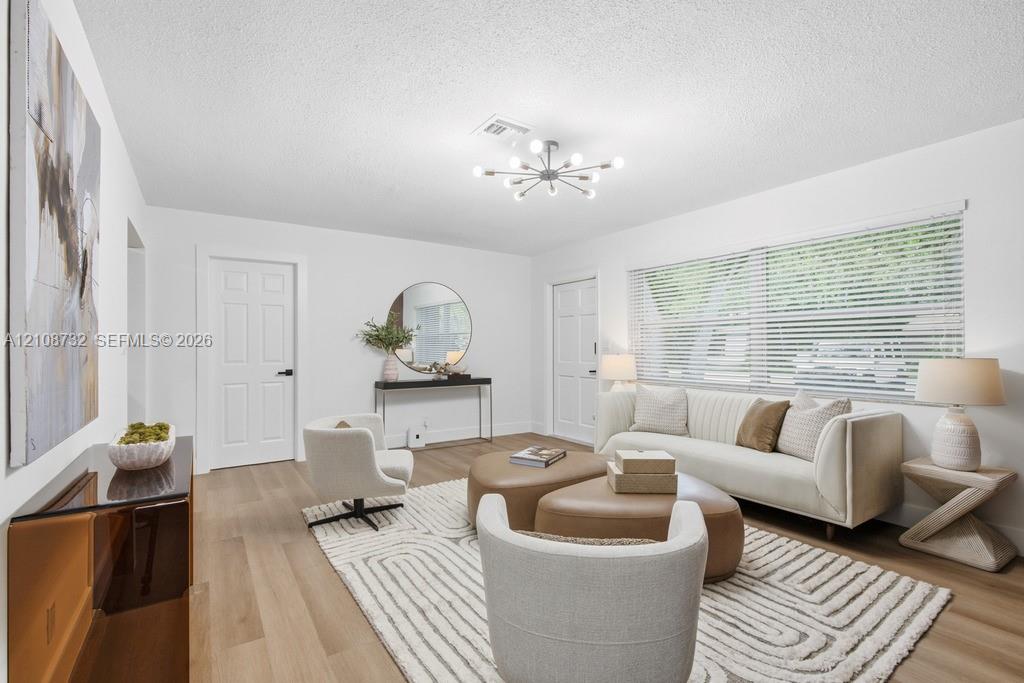 Living area featuring wood-finish flooring, a modern multi-arm sputnik chandelier, and a large window with horizontal blinds