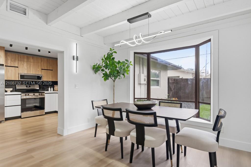 Exposed beam ceiling, light wood-finish flooring, bay window, contemporary linear LED chandelier, and modern wall-mounted accent lighting