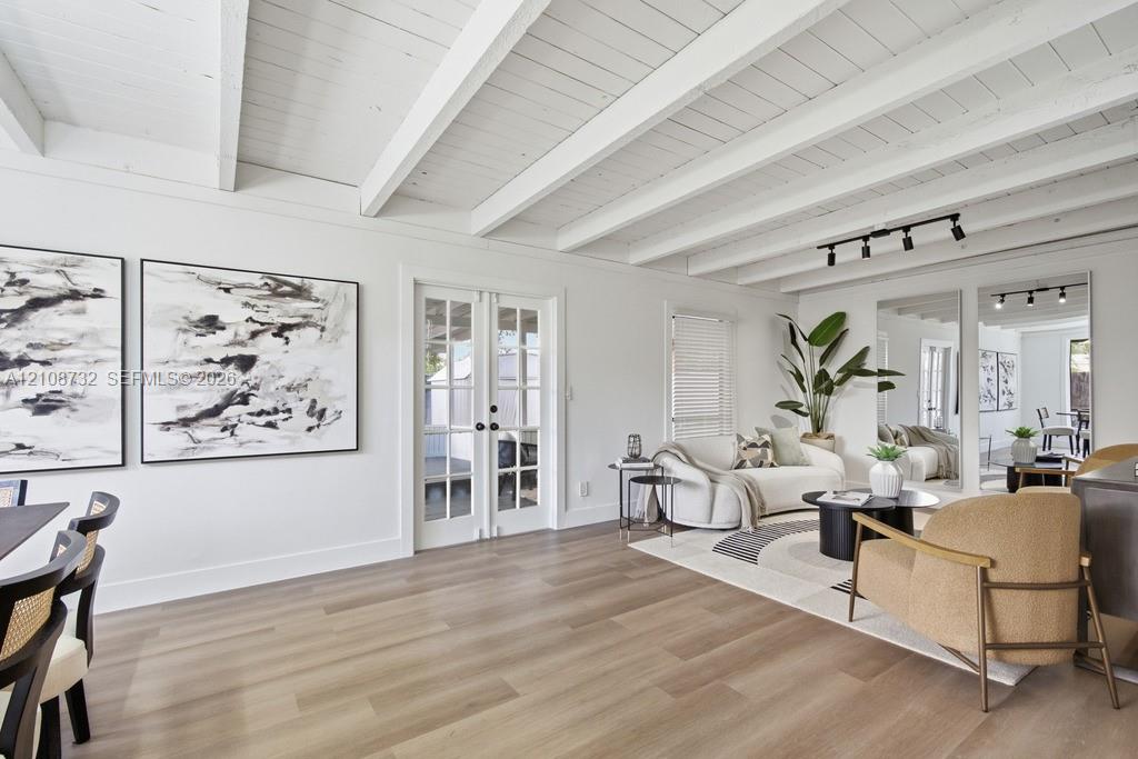 Vaulted ceilings featuring exposed white-painted beams, light wood-finish flooring, glass-paned French doors, and ceiling-mounted track lighting