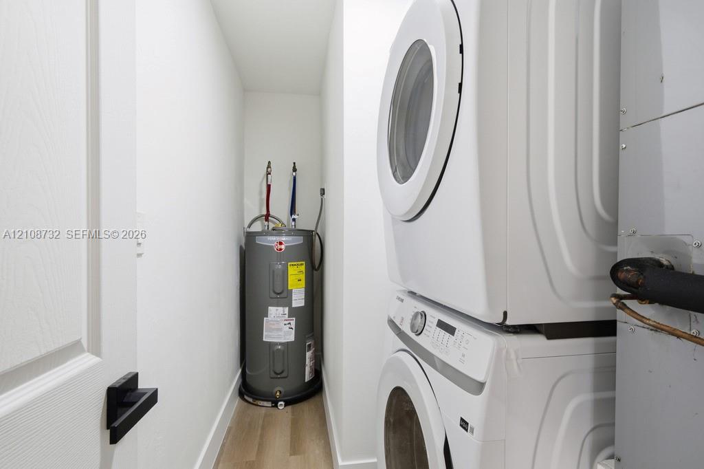 Utility closet featuring stackable laundry appliances, a water heater, and wood-finish flooring