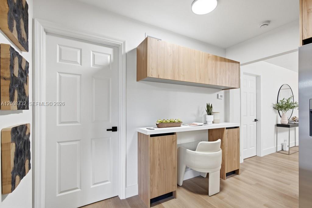 Built-in workstation featuring wood-finish cabinetry, a white countertop, and a wall-mounted overhead cabinet, complemented by wood-finish flooring and paneled interior doors with matte black hardware
