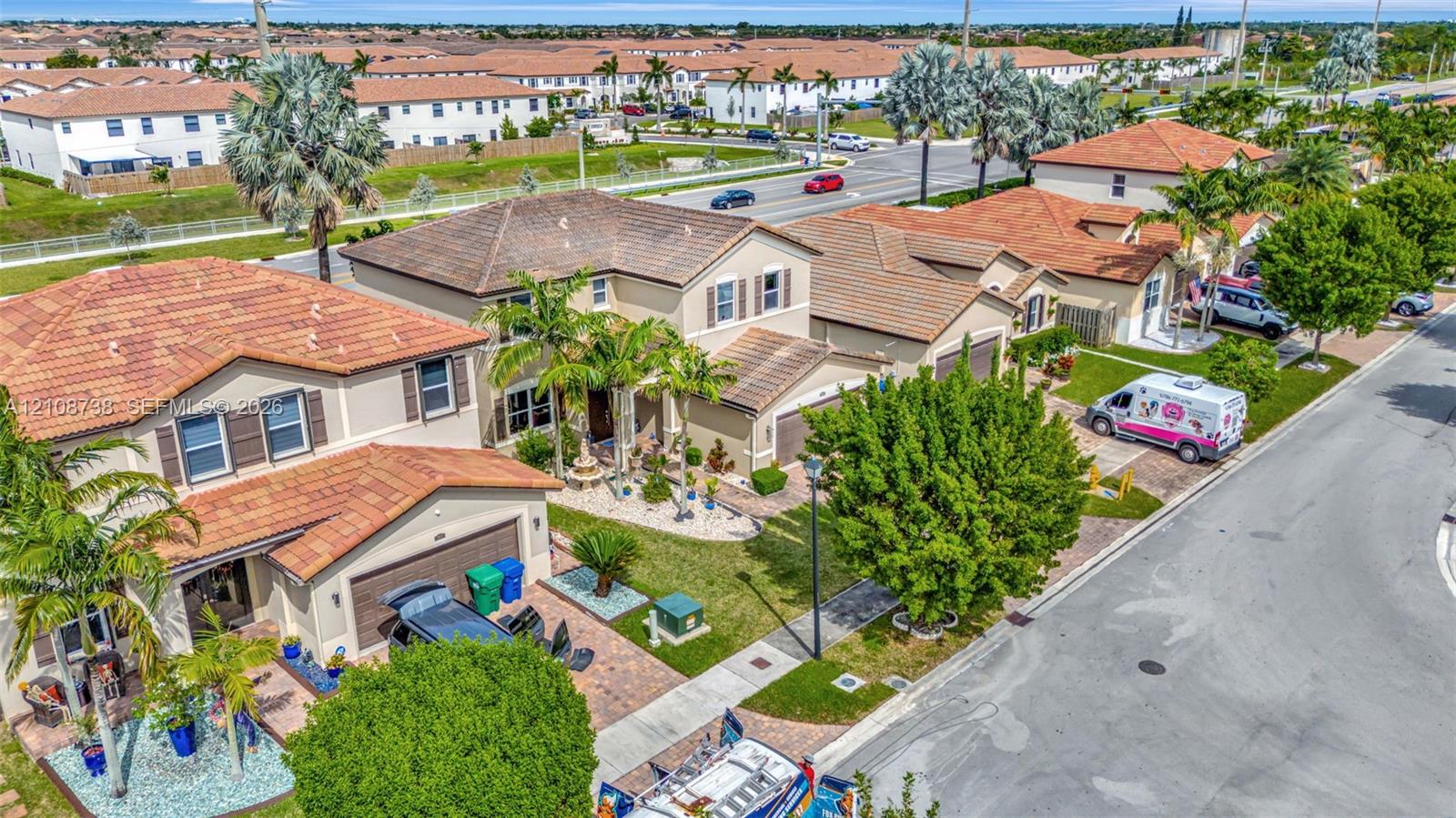 Two-story residence featuring a clay tile roof, paved driveway, multi-car garage, and mature palm landscaping