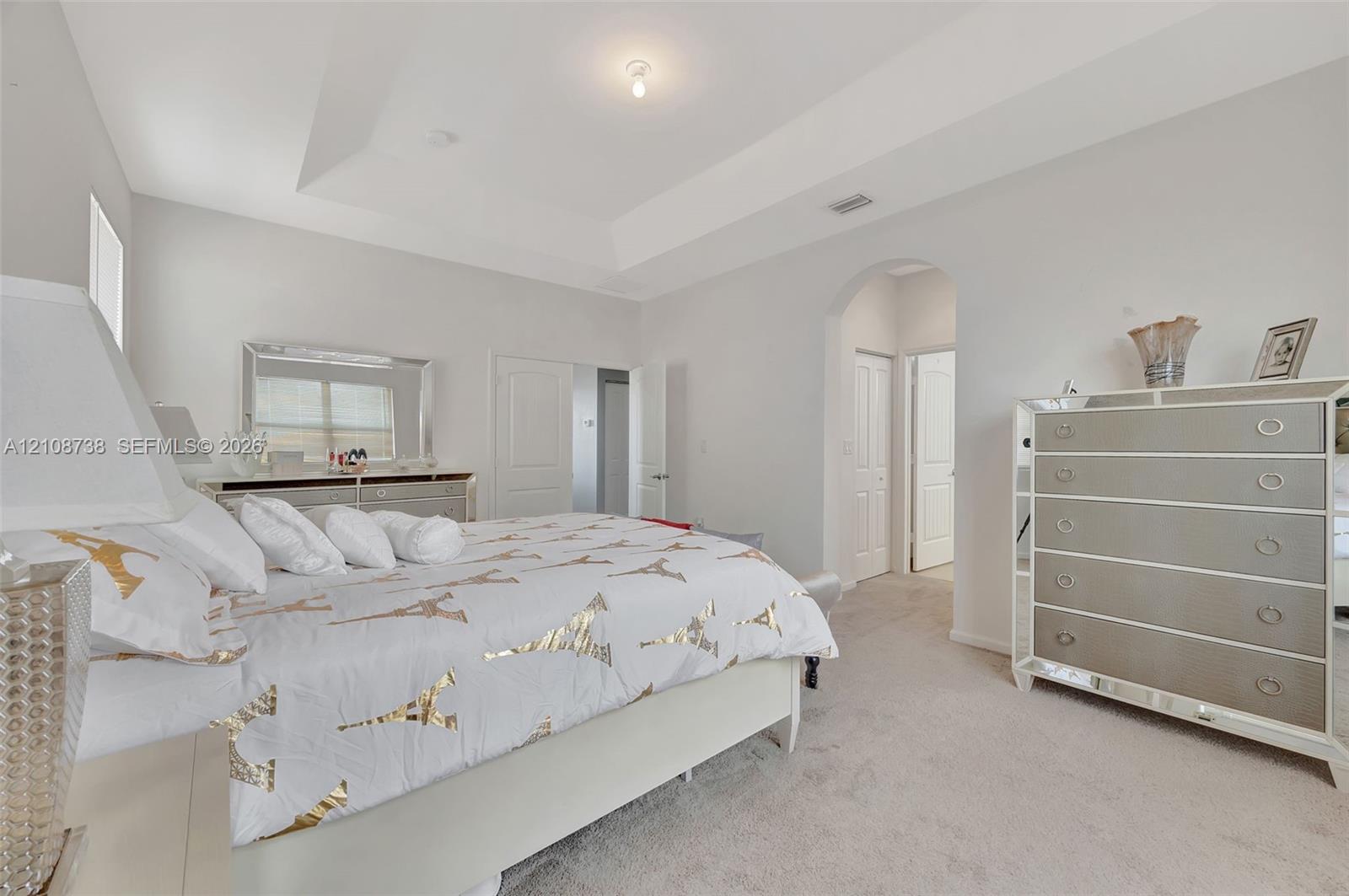 Tray ceiling, neutral wall tones, arched entryway, and neutral carpeted flooring