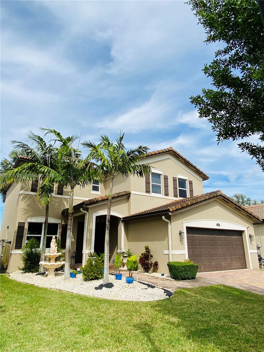 Two-story residence featuring a tile roof, stucco exterior, attached two-car garage, paver driveway, and landscaped front yard with palm trees