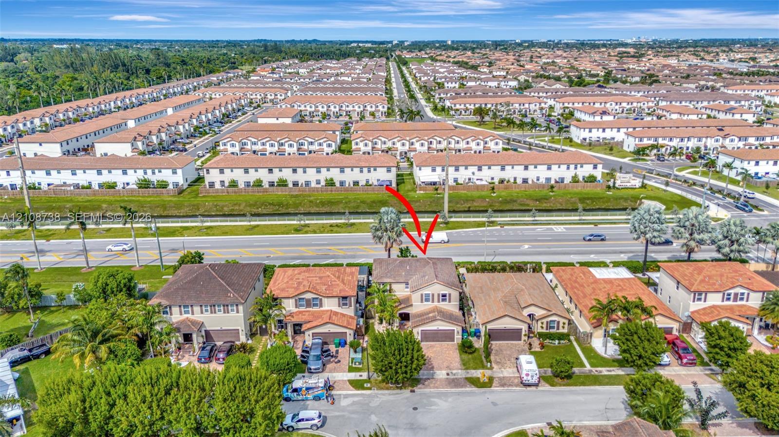 Aerial view of a two-story residence featuring a tile roof, paved driveway, and attached garage, situated in a residential neighborhood with mature landscaping