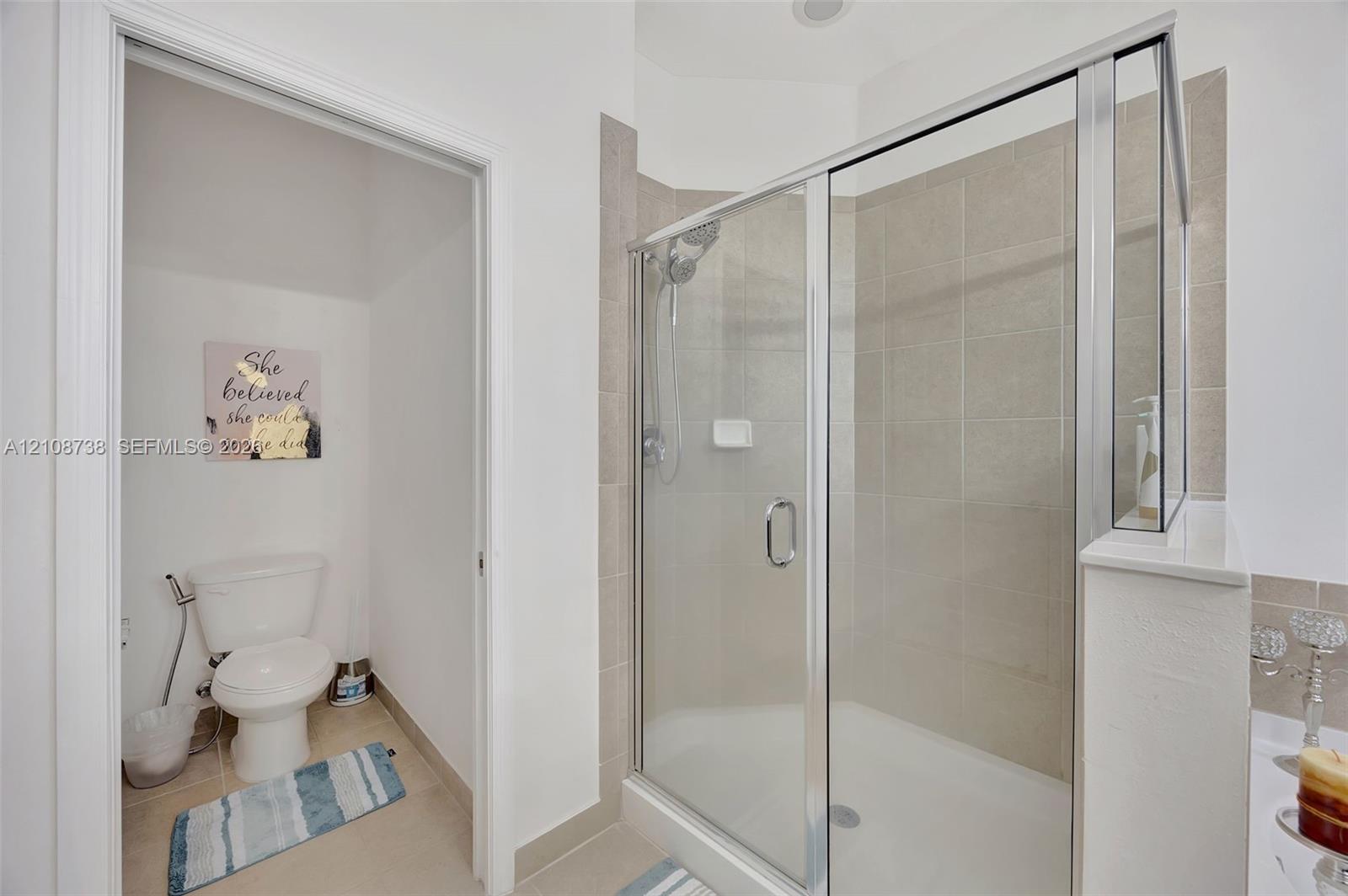 Walk-in shower featuring a glass enclosure, neutral tile surround, and adjustable handheld showerhead, accompanied by a separate water closet area