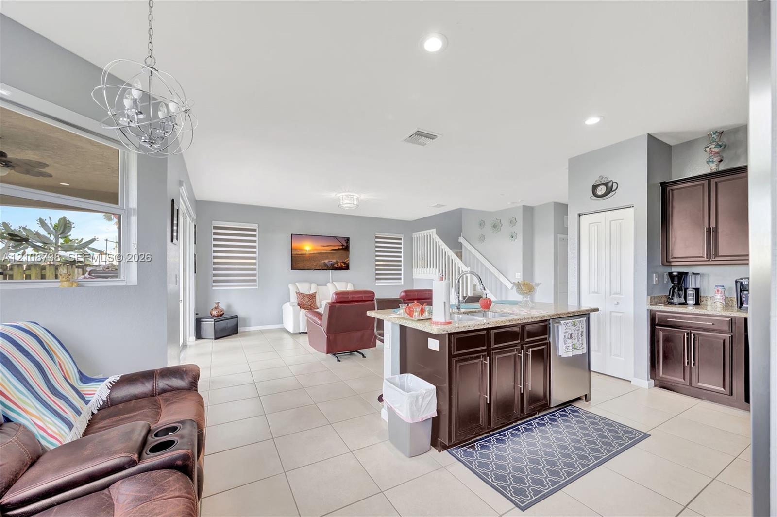 Open-concept interior featuring large-format tile flooring, a kitchen island with stone surfacing, espresso-toned cabinetry, recessed lighting, and a modern sculptural pendant fixture