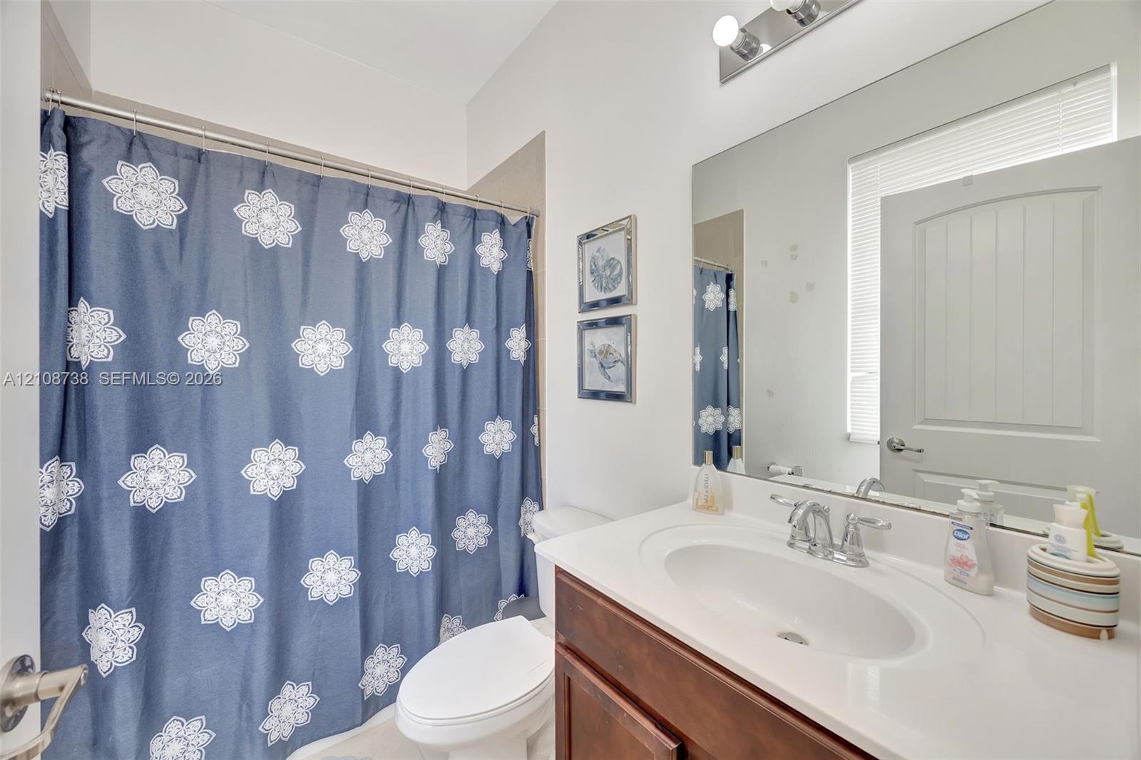 Bathroom featuring a vanity with wood-finish cabinetry, an integrated oval sink, a full-width mirror, and a wall-mounted light fixture
