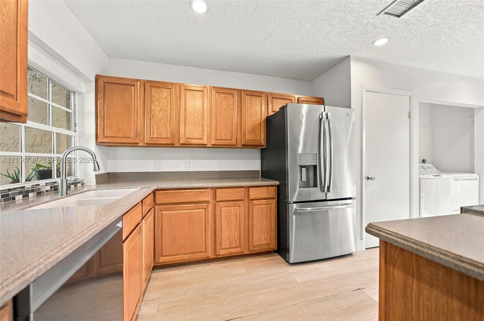 Kitchen featuring wood cabinetry, stainless steel refrigerator, stone-finish countertops, dual-basin undermount sink, and wood-finish flooring