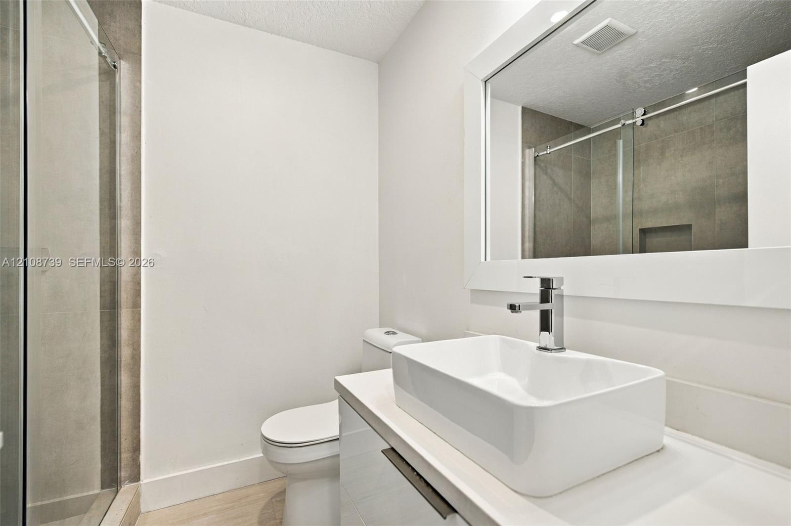 Bathroom featuring a rectangular vessel sink, wall-mounted mirror with a white frame, gloss-finish vanity, glass-enclosed shower, and polished chrome fixtures
