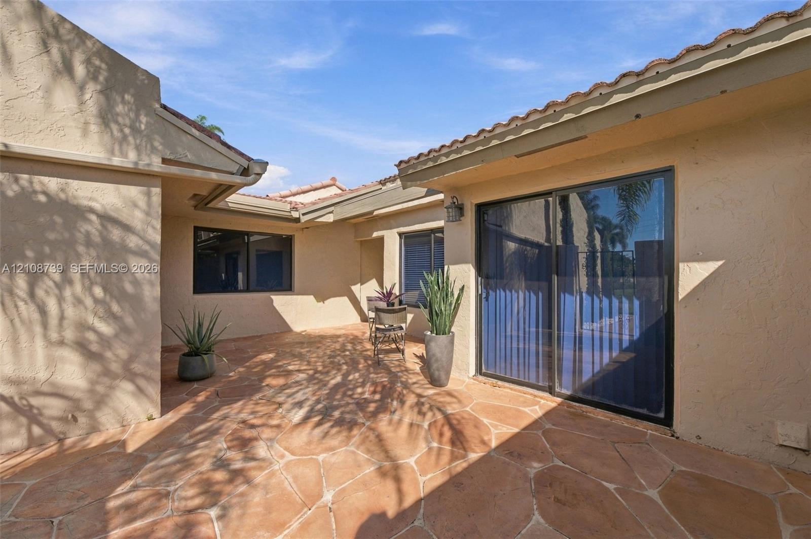 Private courtyard featuring flagstone paving, stucco exterior walls, sliding glass door, and tiled roof