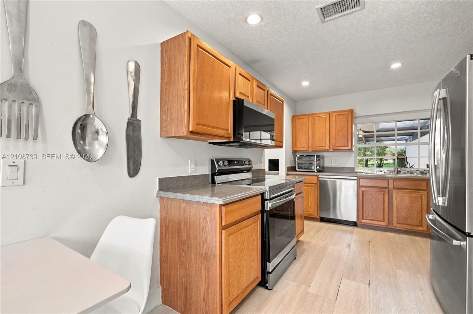 Kitchen featuring light wood-finish cabinetry, solid-surface countertops, recessed lighting, and stainless steel appliances