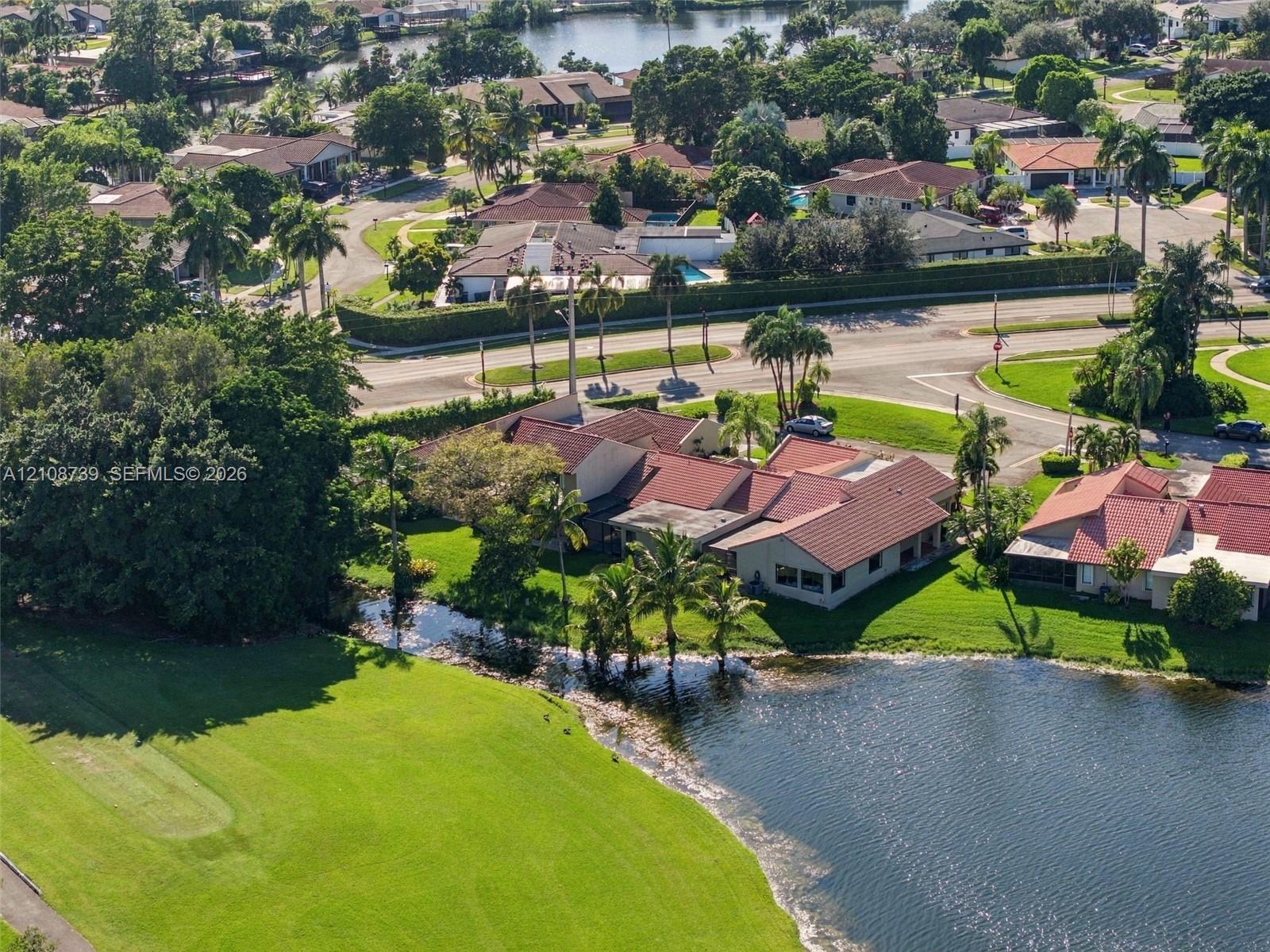 Waterfront property featuring a tile roof, mature palms, expansive lawn, and direct proximity to a golf course
