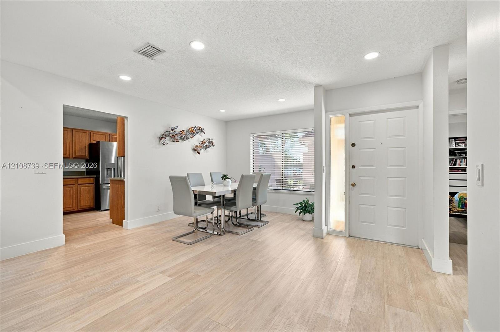 Open-concept interior featuring light wood-finish flooring, recessed lighting, and a six-panel entry door with a side light