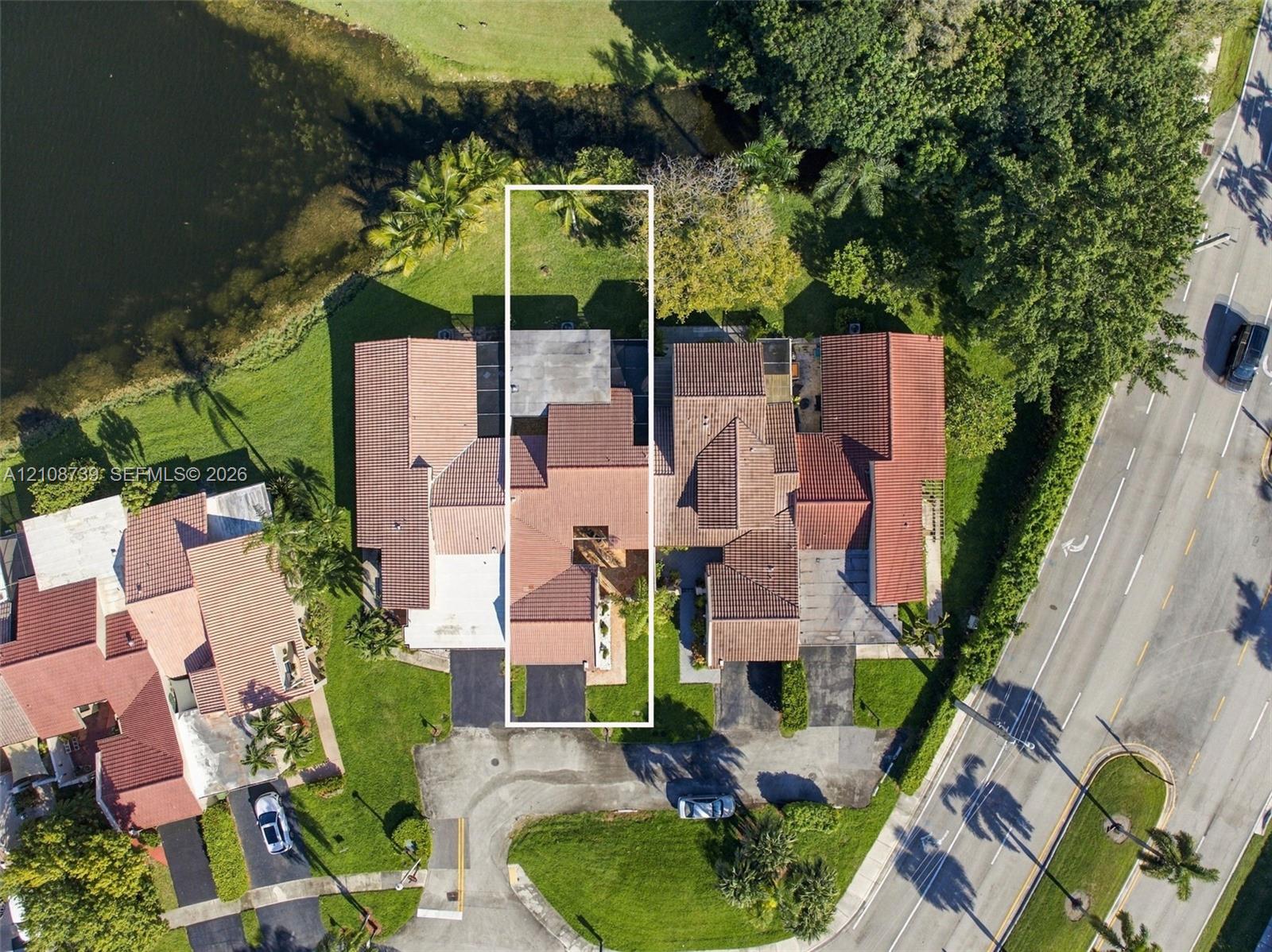 Aerial perspective of property featuring a tile roof, paved driveway, and waterfront lot with mature landscaping