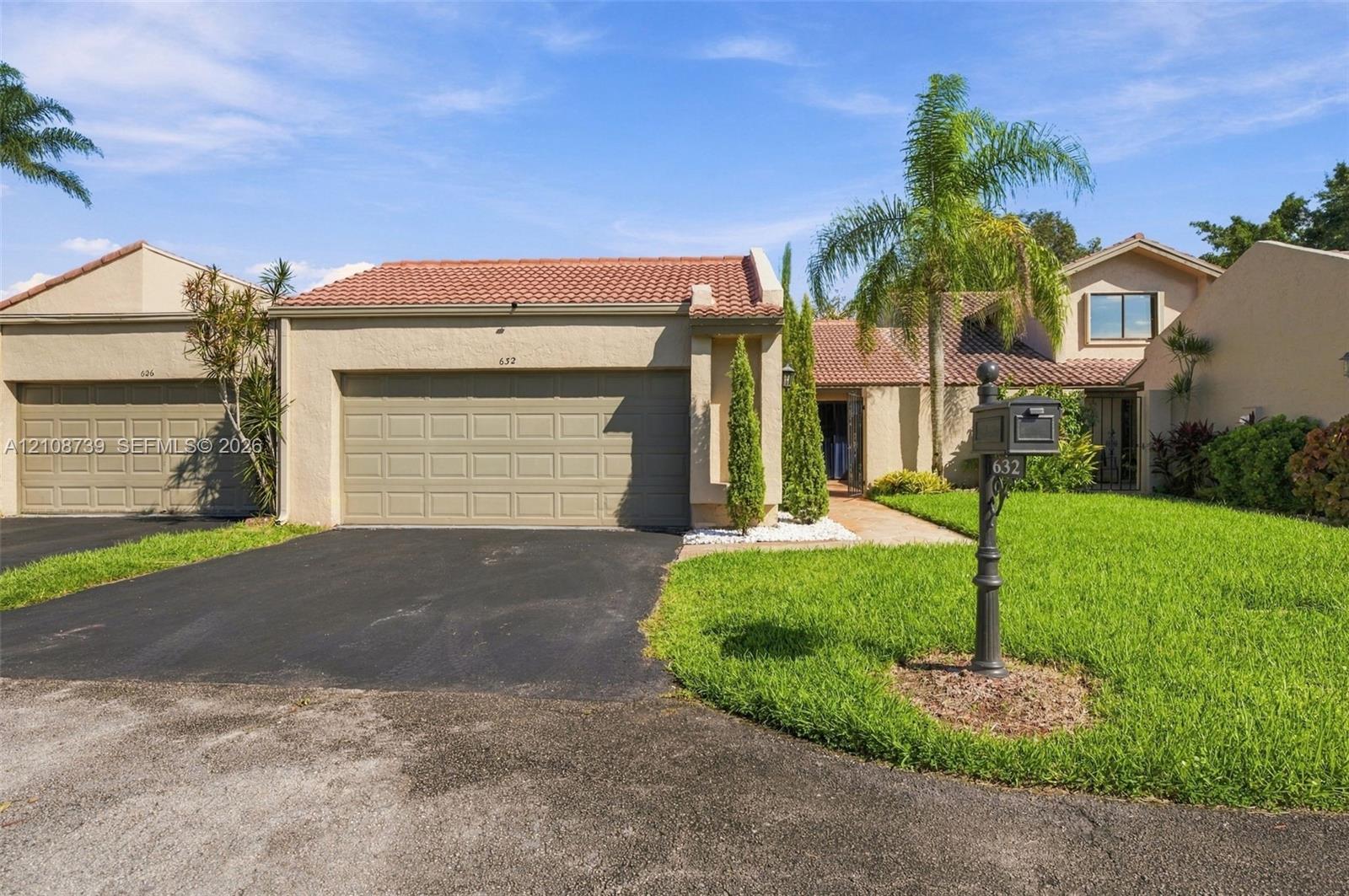 Stucco exterior featuring a clay tile roof, two-car garage, manicured lawn, and mature landscaping