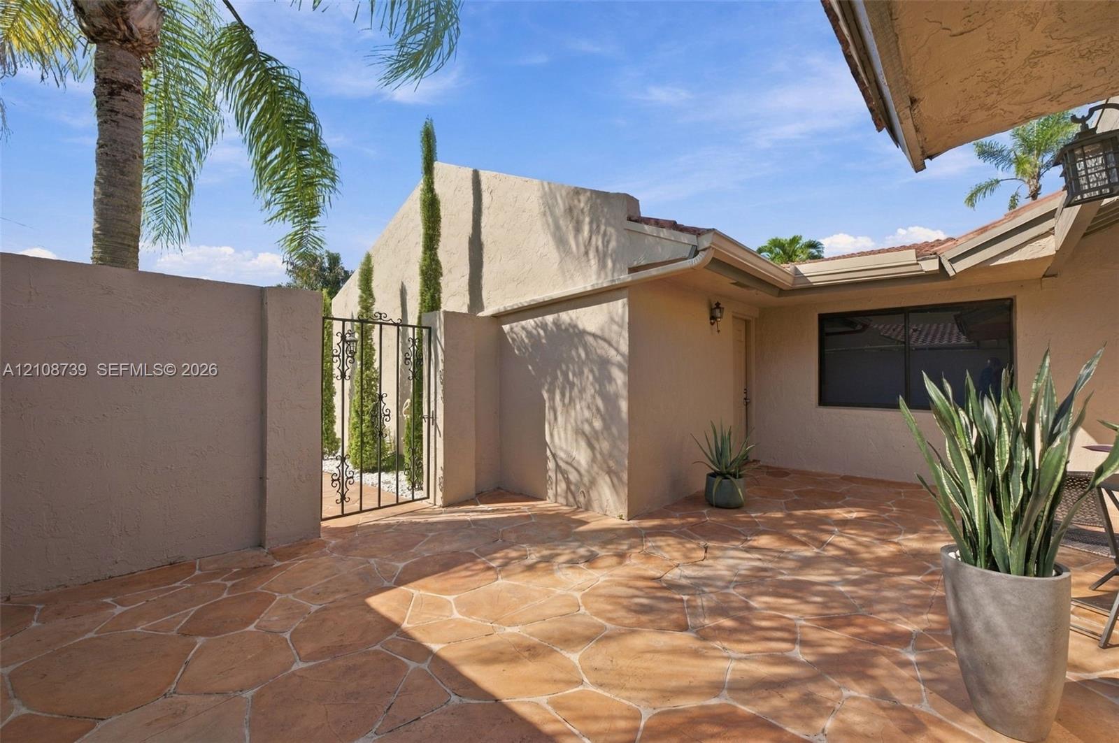 Stucco exterior featuring an enclosed flagstone courtyard, wrought-iron gate, and integrated wall-mounted lighting