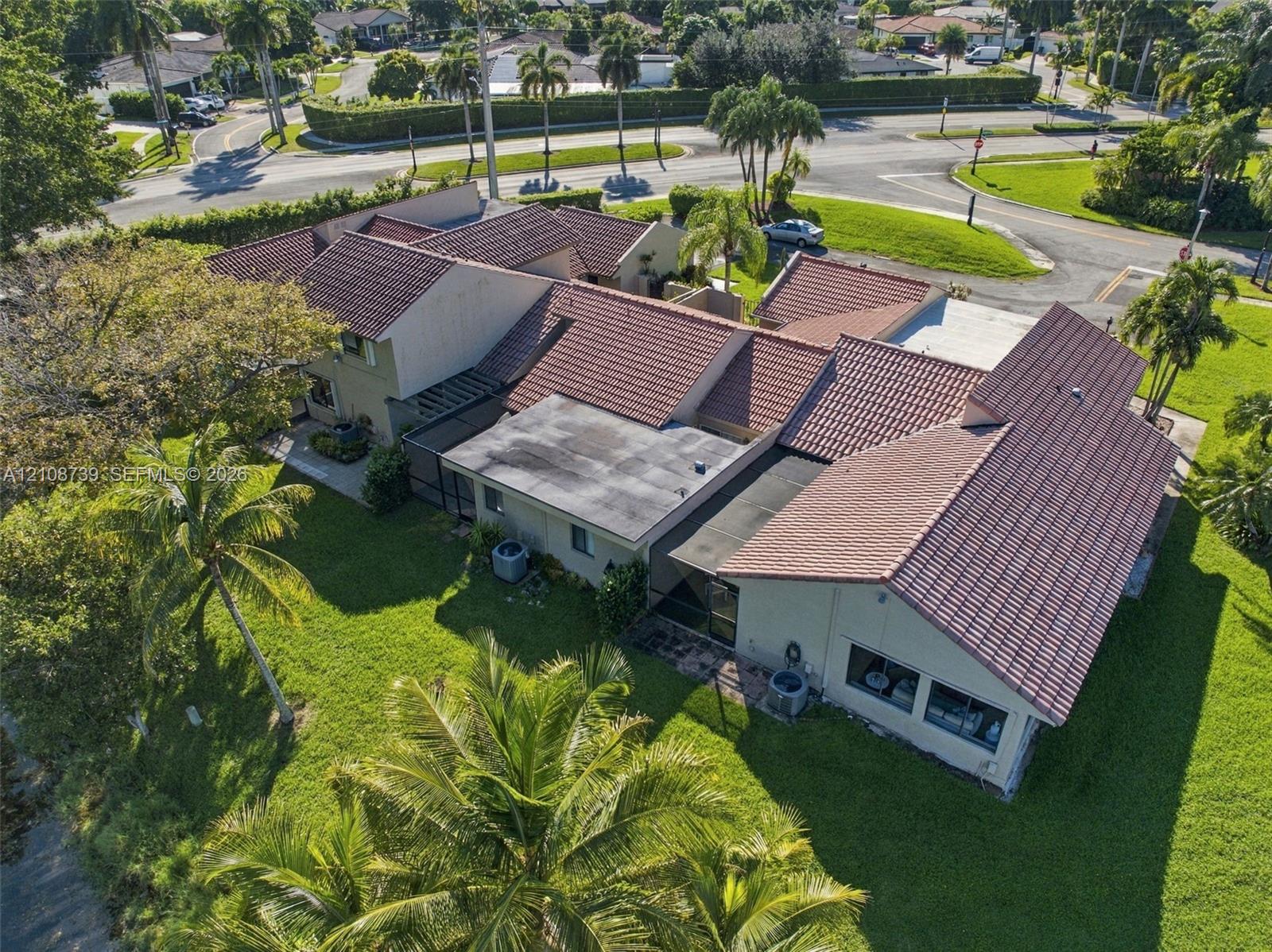 Aerial perspective of a property featuring a multi-gabled tile roof, concrete-block construction, and expansive lawn area with mature palm trees