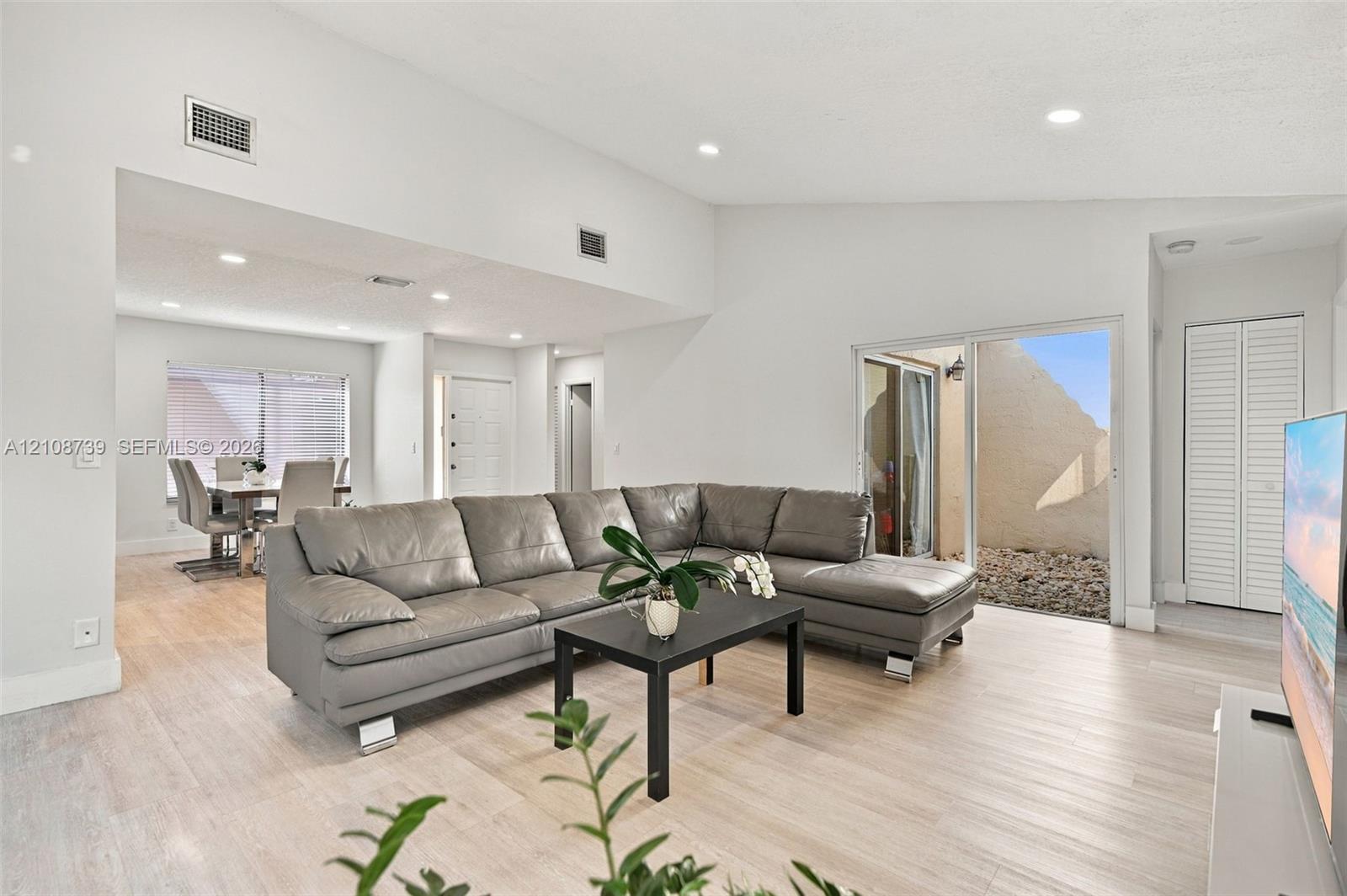 Vaulted ceilings, light-tone wood-finish flooring, recessed lighting, and a sliding glass door providing external access