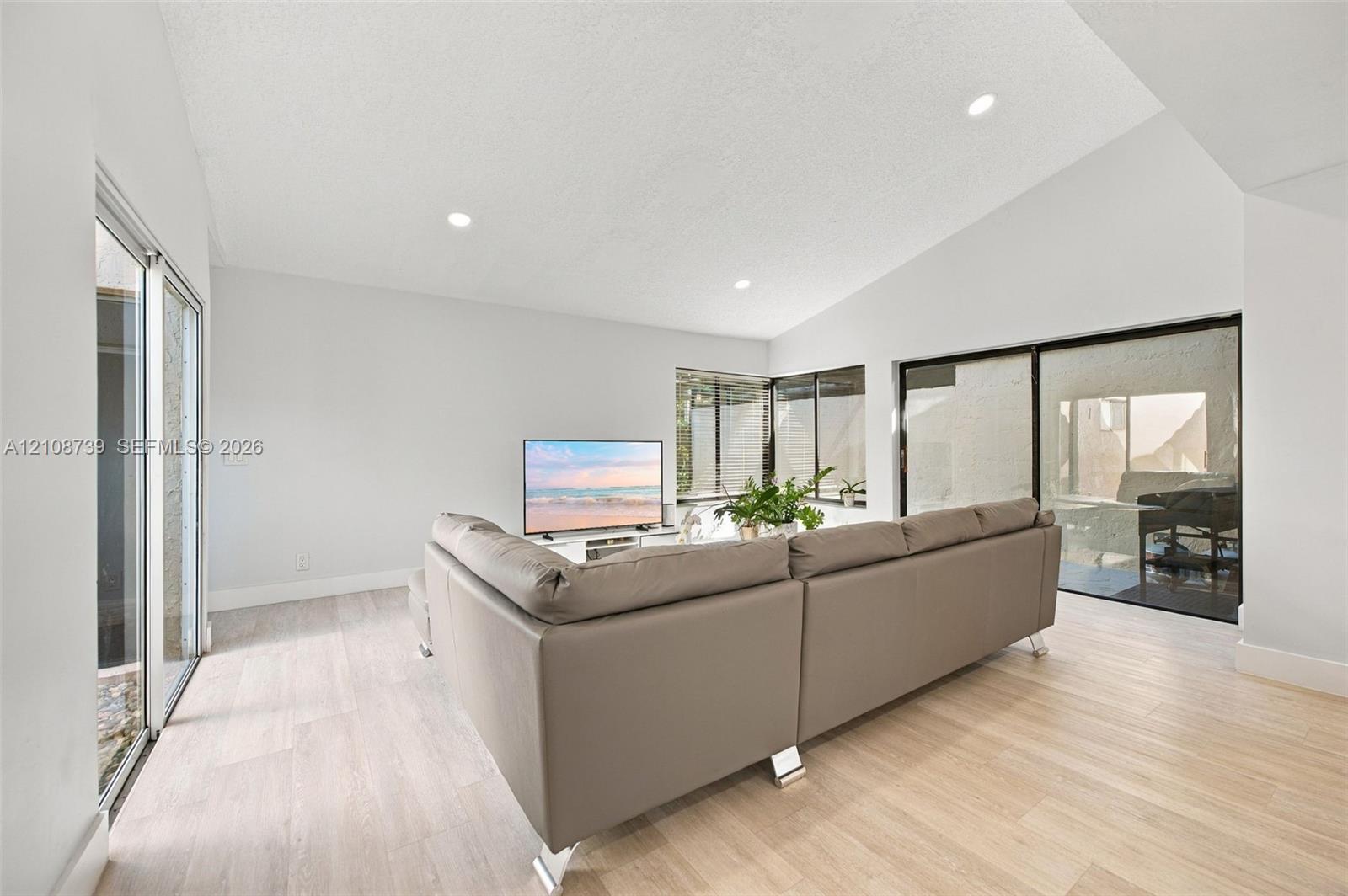 Vaulted ceilings, wood-finish flooring, recessed lighting, and multiple sliding glass doors