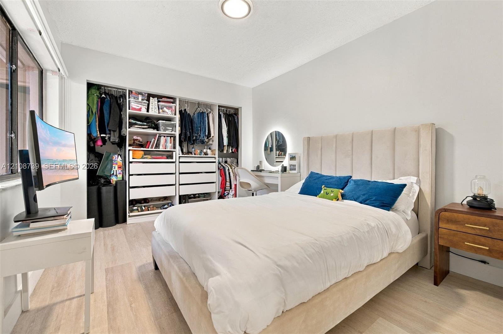 Light-filled room featuring wood-finish flooring, a large window, and custom built-in closet cabinetry with integrated drawers and shelving