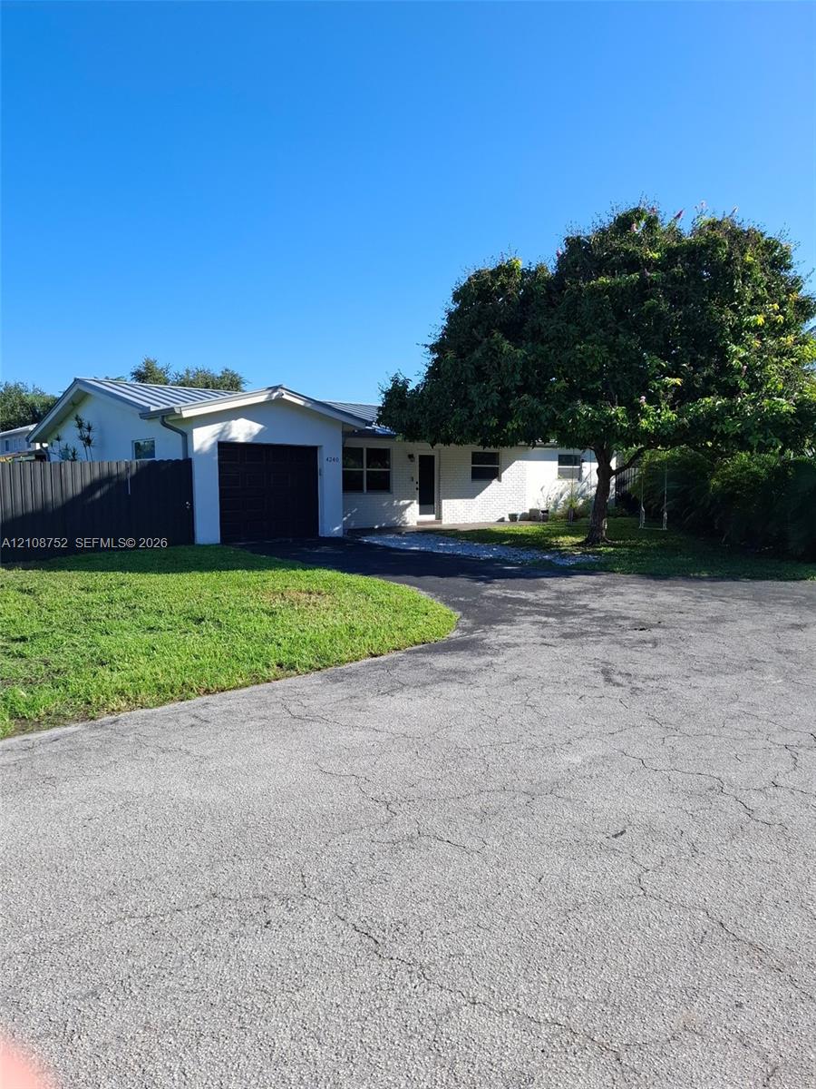 Single-story residence featuring a metal roof, attached garage, paved driveway, and mature landscaping Single-story residence featuring a metal roof, attached garage, paved driveway, and mature landscaping