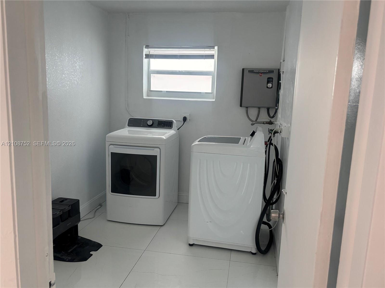 Laundry area featuring neutral-toned tile flooring, white walls, and a window with blinds