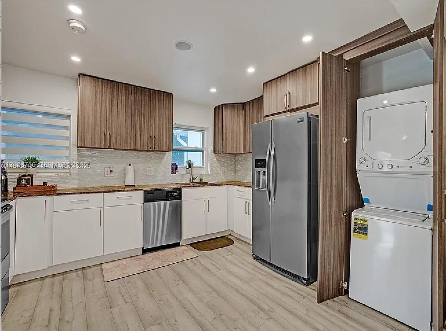 Kitchen featuring two-tone upper and lower cabinetry, stainless steel appliances, stone-surface countertops, recessed lighting, and integrated laundry closet