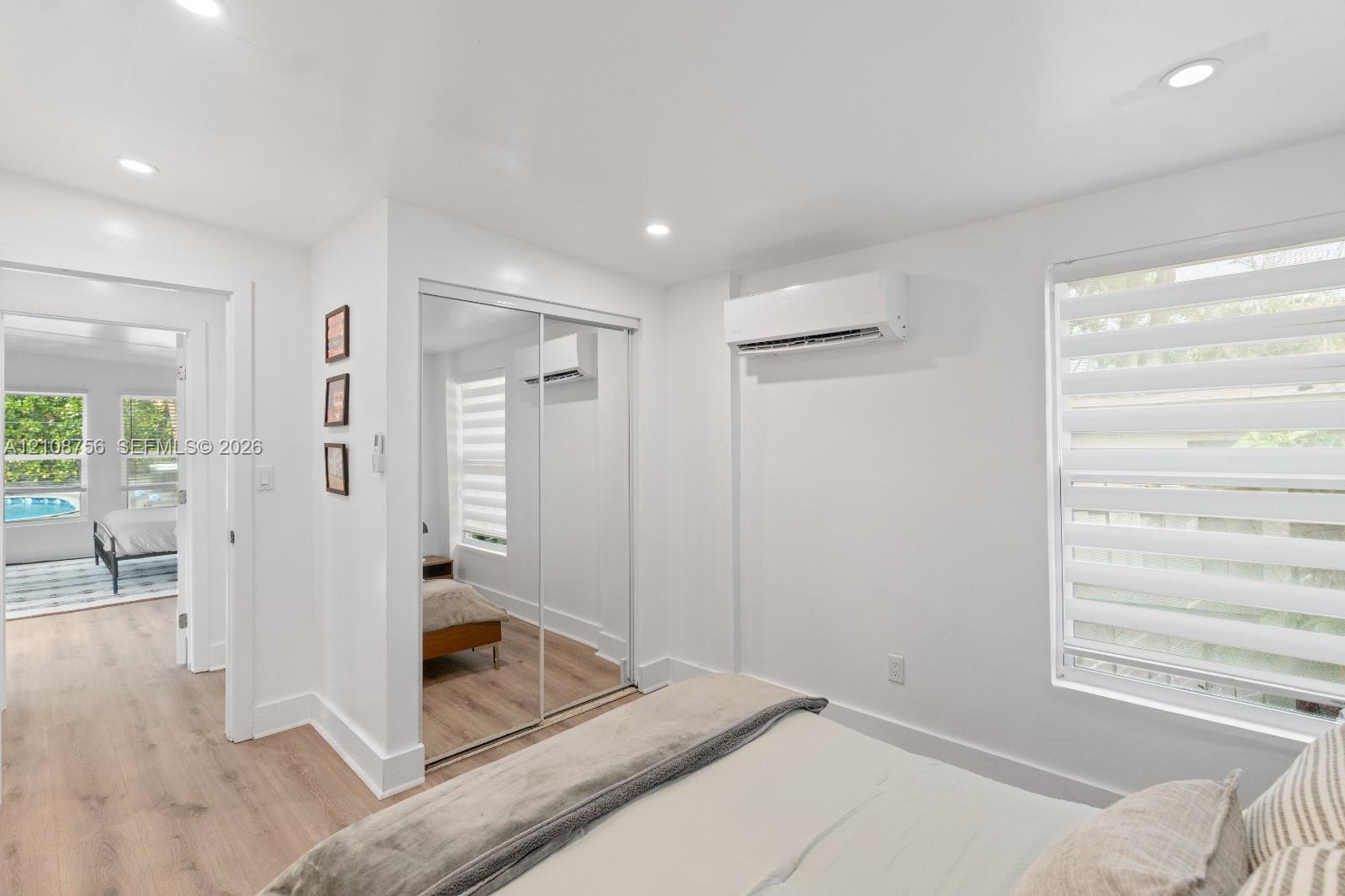 Bedroom featuring wood-finish flooring, recessed lighting, wall-mounted ductless air conditioning unit, and sliding mirrored closet doors
