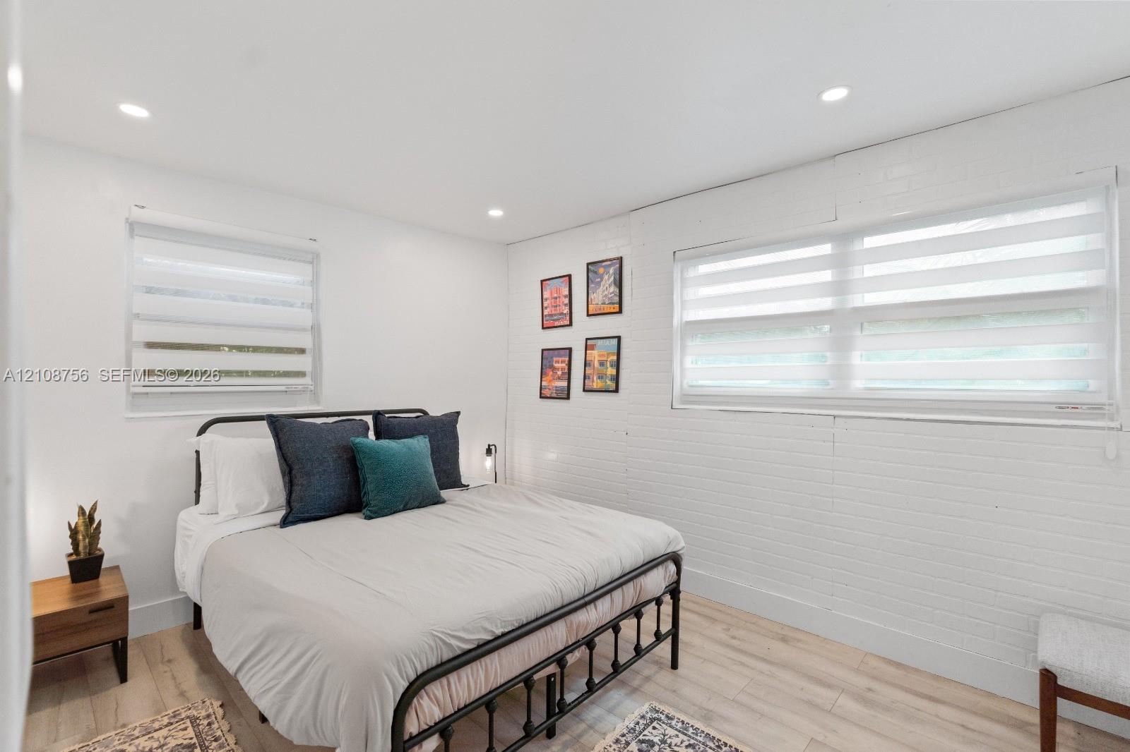 Bright interior featuring white painted brick walls, wood-finish flooring, recessed lighting, and dual windows with fitted shades