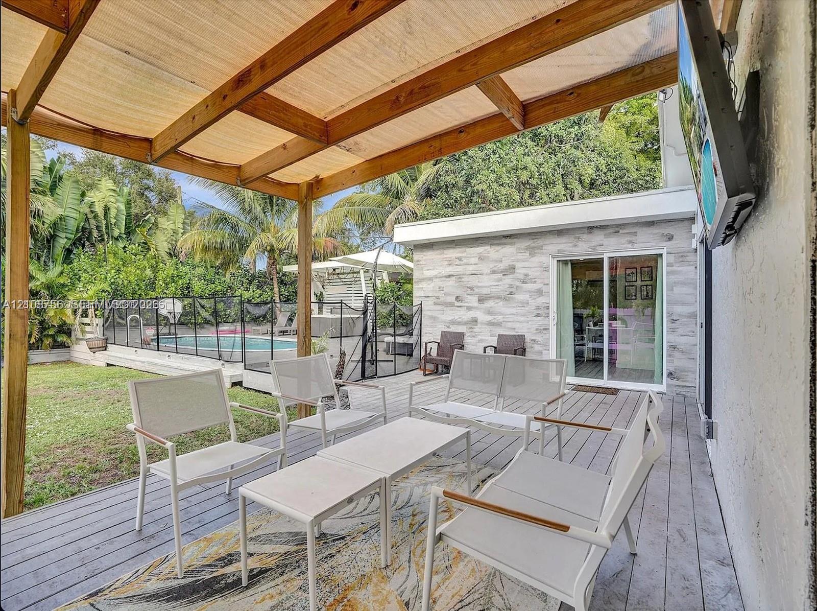 Covered wooden pergola, expansive wood-finish deck, exterior wall with stone-style veneer, sliding glass door, and fenced in-ground pool