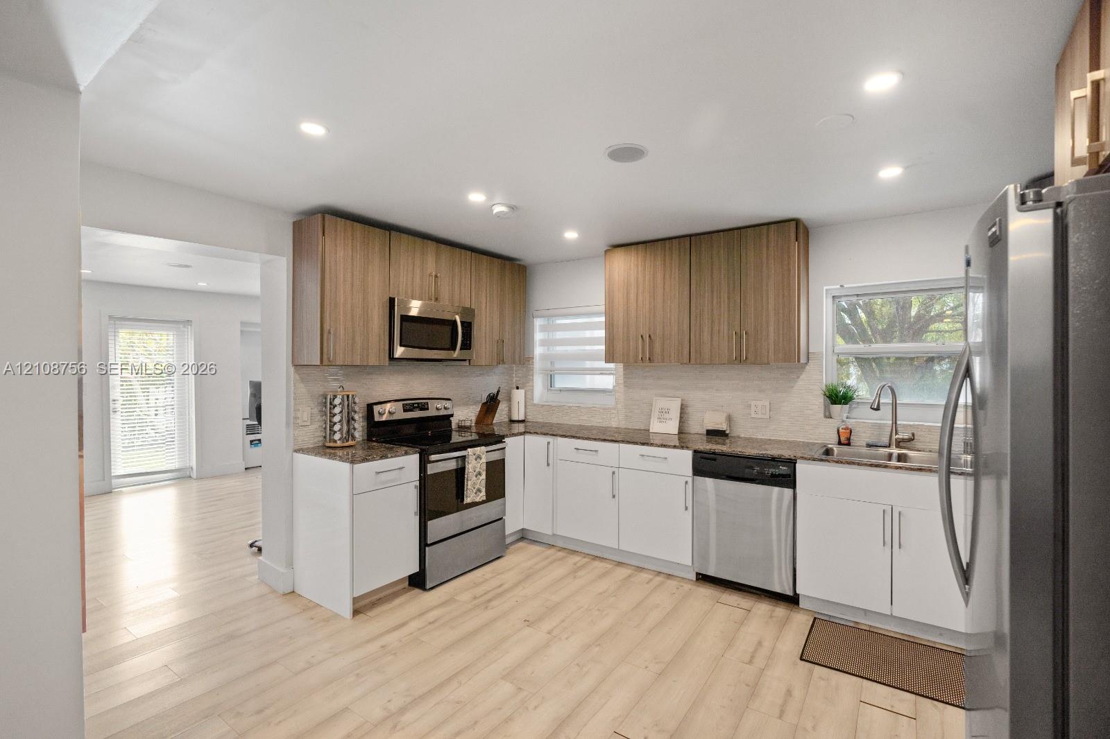 Kitchen featuring two-tone cabinetry, stone countertops, stainless steel appliances, wood-finish flooring, and recessed lighting