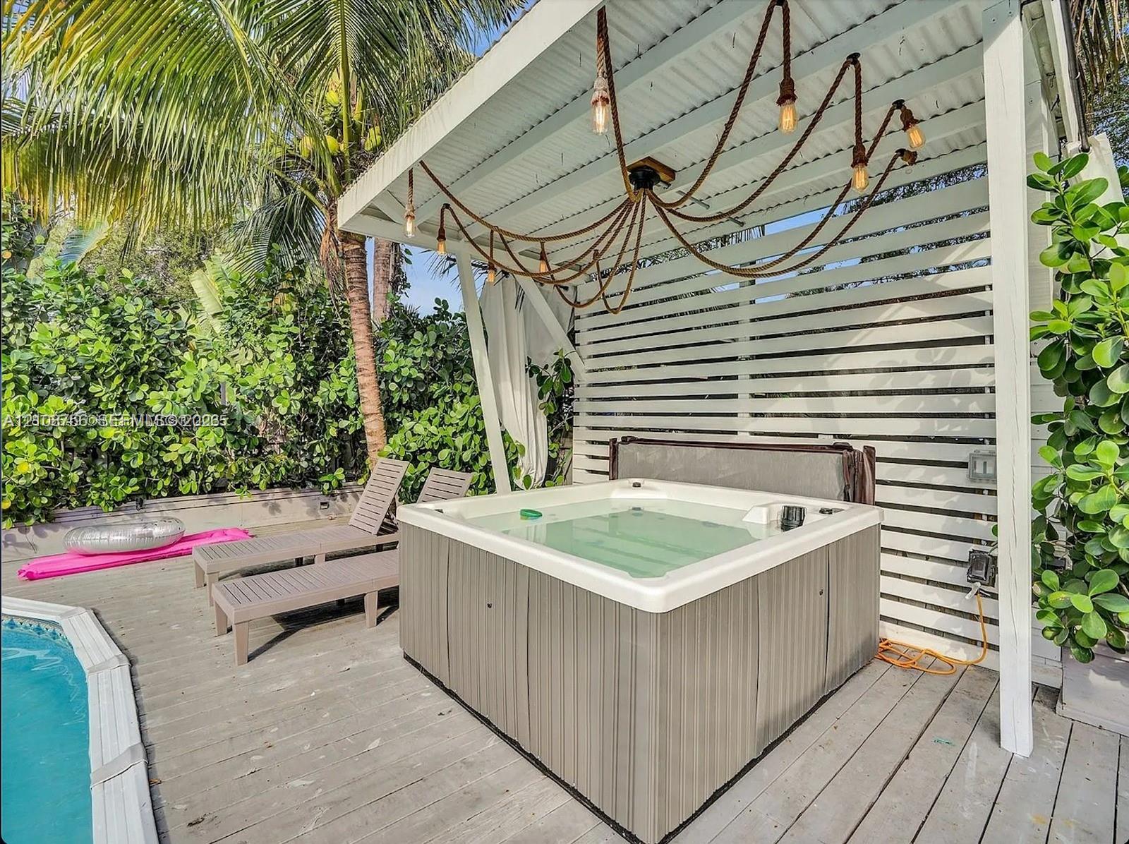 Outdoor deck featuring a wood-finish floor, a covered spa with a horizontal slat privacy screen, and a custom rope-style chandelier Outdoor deck featuring a wood-finish floor, a covered spa with a horizontal slat privacy screen, and a custom rope-style chandelier