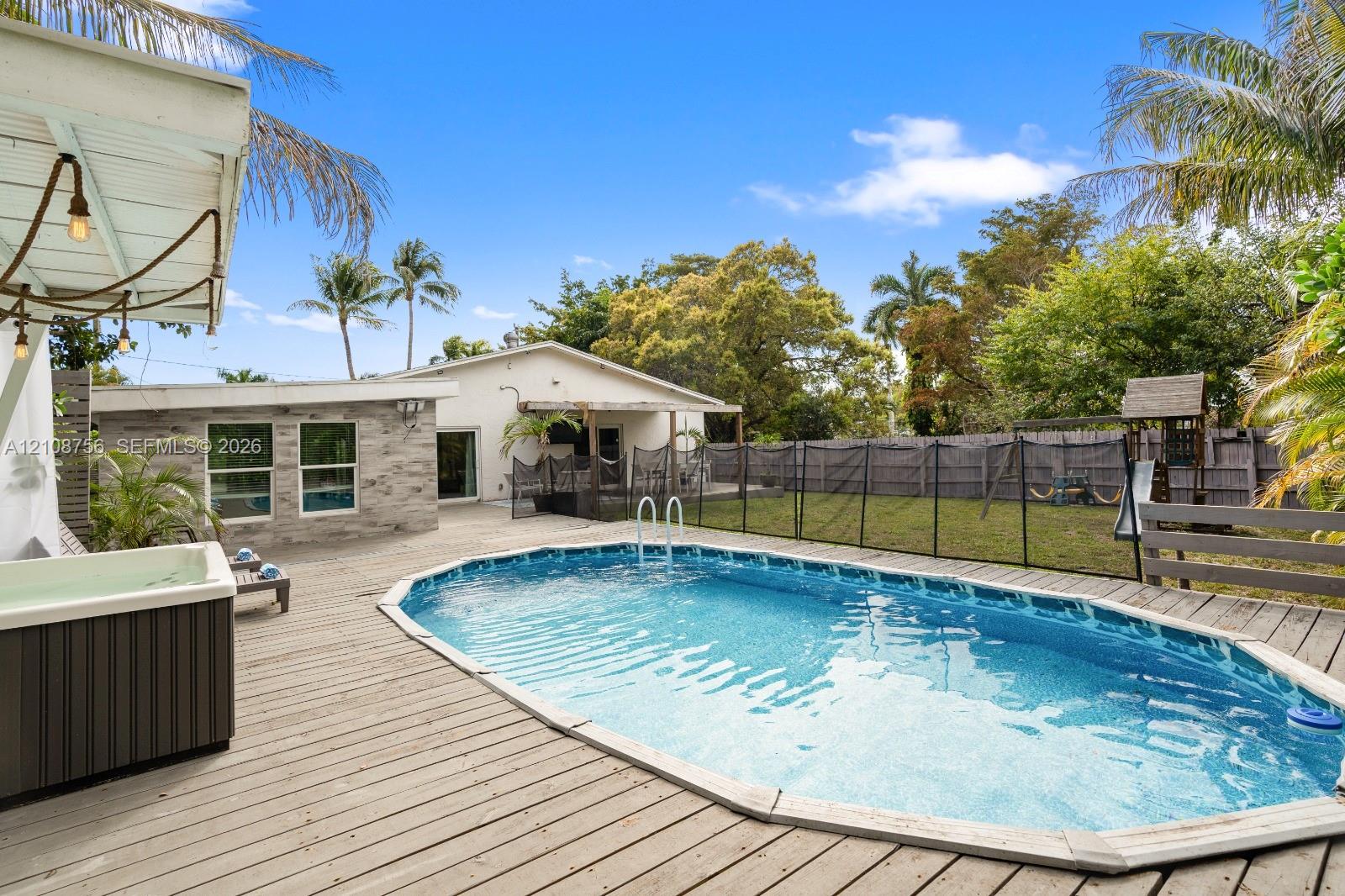 Backyard featuring an inground swimming pool, wood-finish decking, integrated spa, and full-perimeter fencing