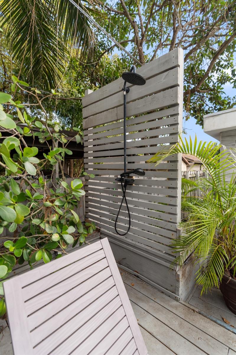 Outdoor shower featuring a matte black rainfall showerhead with a handheld sprayer, mounted on a horizontal wood-slat privacy screen set atop wood decking