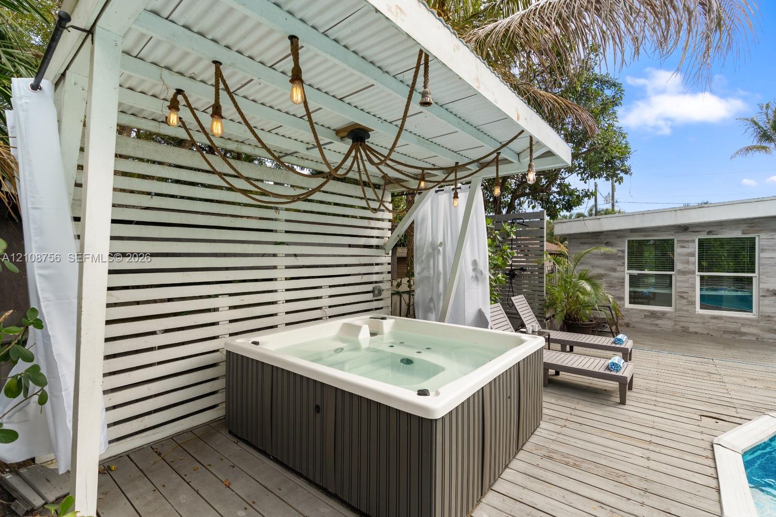 Outdoor space featuring a covered hot tub, horizontal slat privacy screen, suspended pendant lighting, and wood decking Outdoor space featuring a covered hot tub, horizontal slat privacy screen, suspended pendant lighting, and wood decking