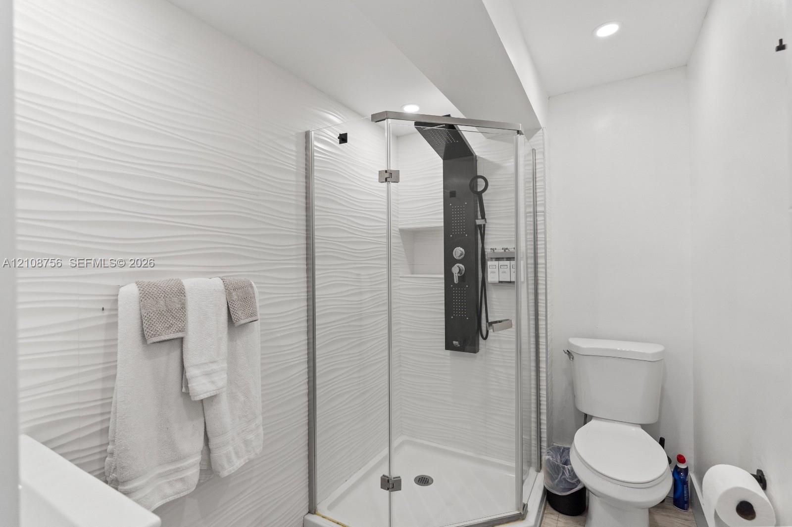 Corner glass shower enclosure featuring a multi-jet shower panel, recessed wall niche, and white textured tile surround