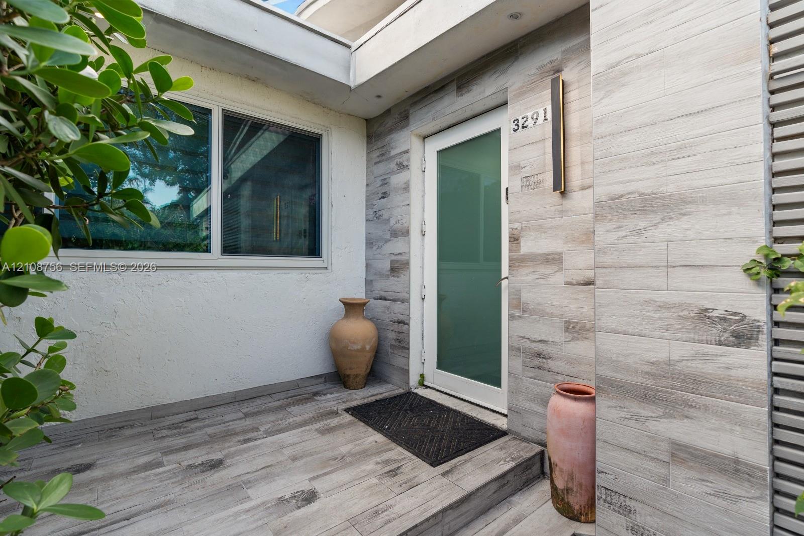 Entry featuring wood-finish tile flooring, textured stucco wall, vertically-oriented exterior wall cladding, and an opaque glass-panel door with integrated linear lighting