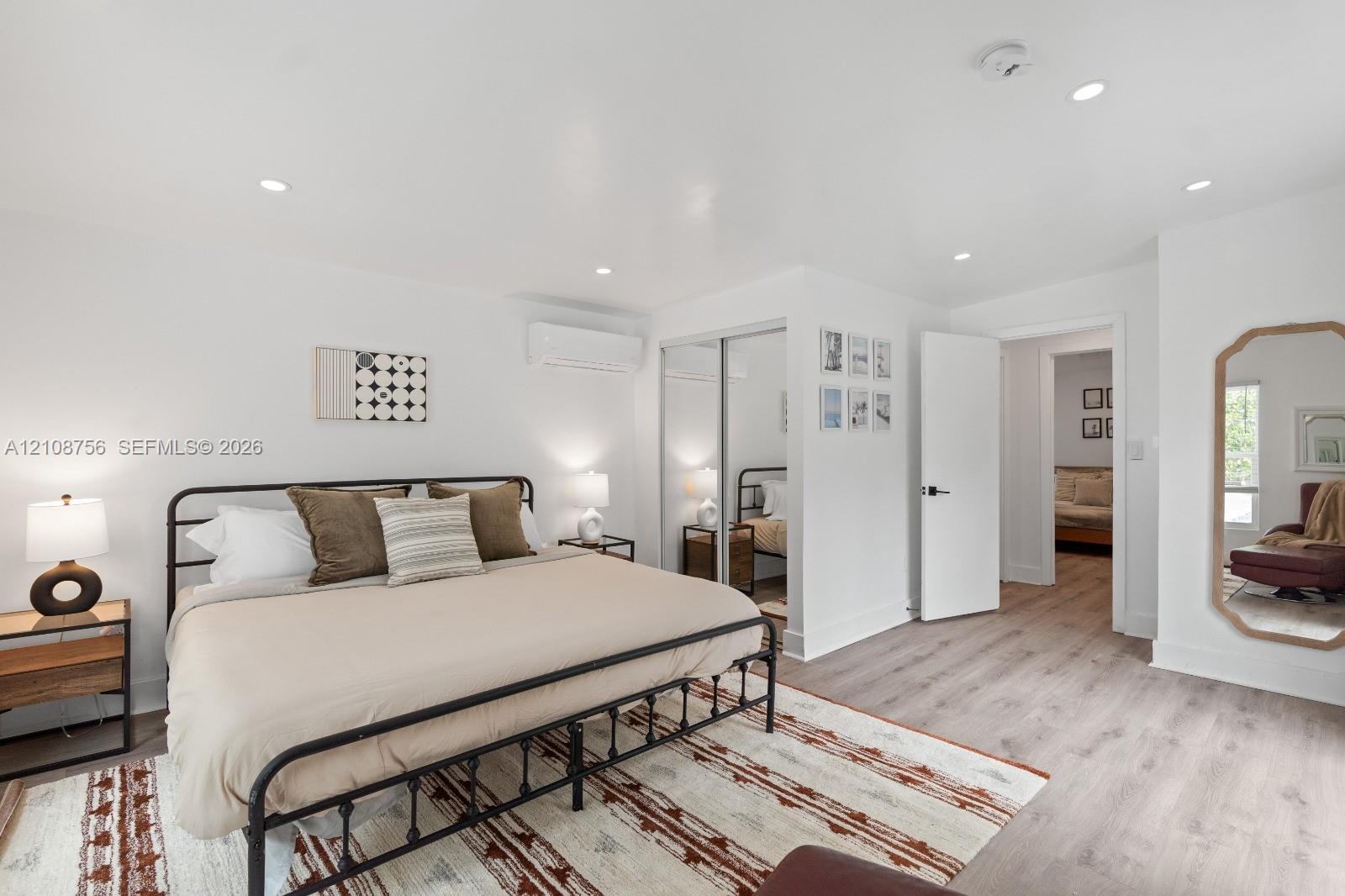 Room featuring wood-finish flooring, recessed lighting, wall-mounted ductless air conditioning unit, and sliding mirror-paneled closet doors