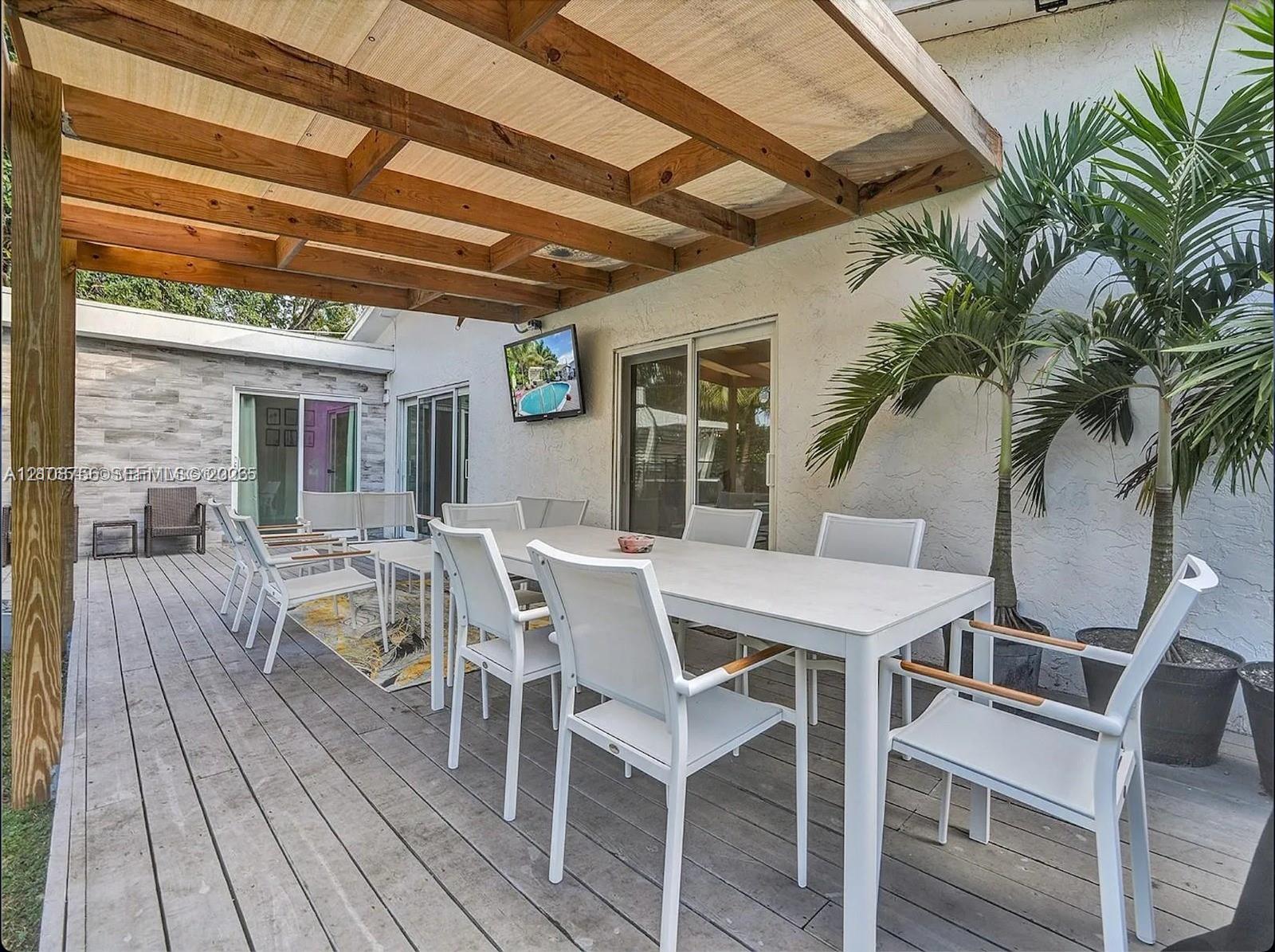 Covered outdoor deck featuring natural wood framing, plank-style decking, textured stucco exterior walls, and sliding glass doors
