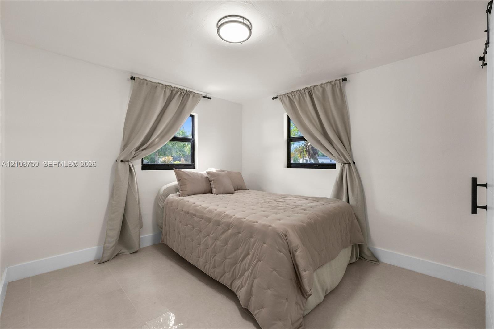 Neutral-toned tile flooring, dual windows with dark frames, and a flush-mount circular ceiling light fixture