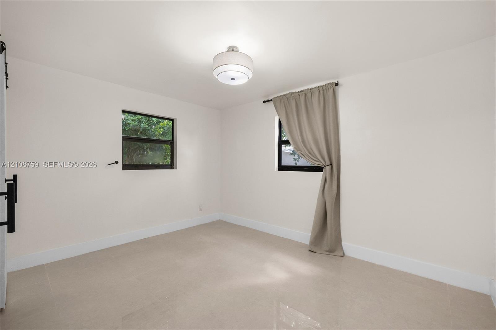 Neutral-toned tile flooring, dual windows with dark frames, and a modern drum-style ceiling light fixture
