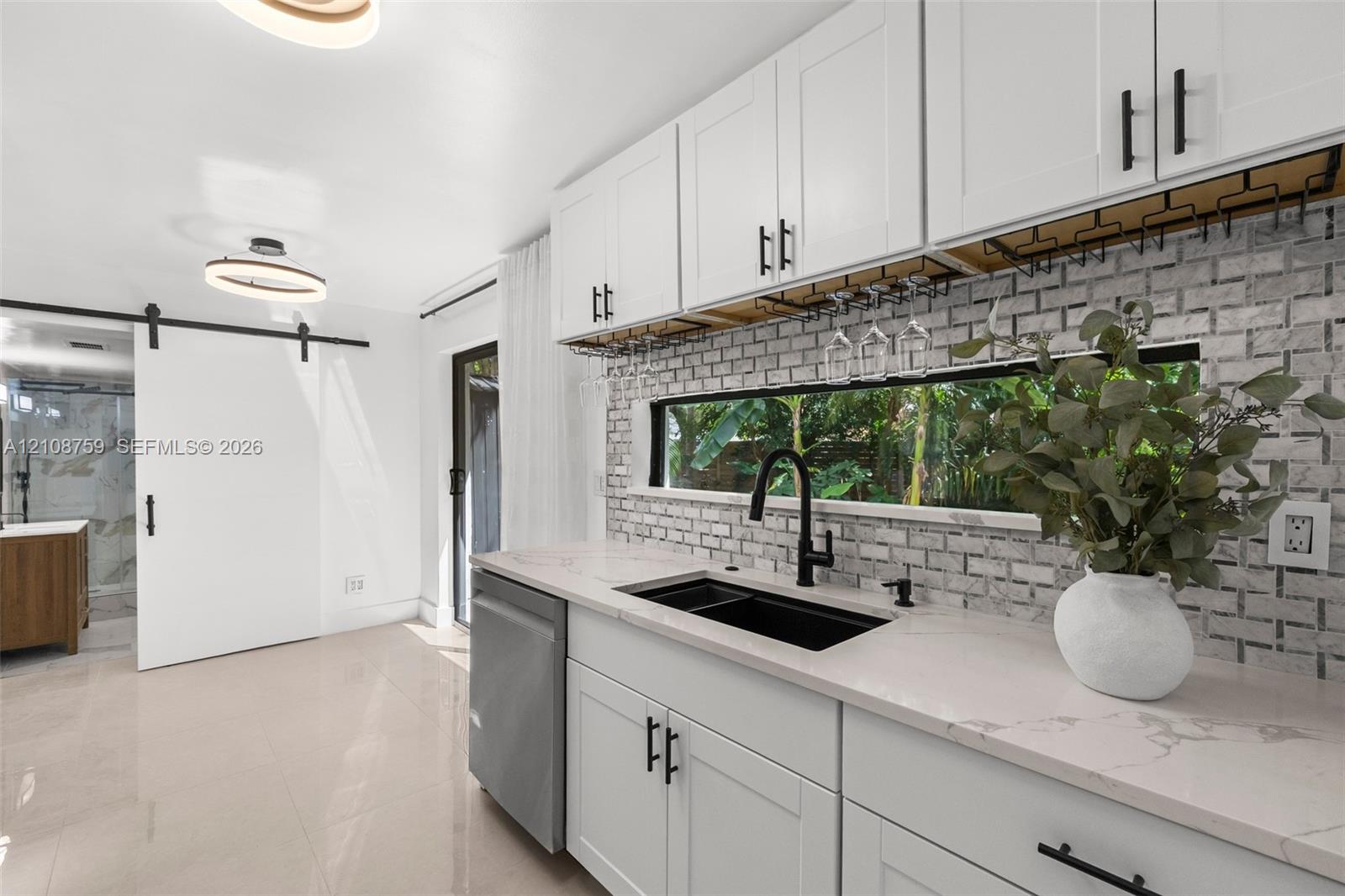Kitchen featuring white shaker cabinetry, stone-look countertops, a mosaic tile backsplash, black hardware, and an undermount sink with a matte black faucet