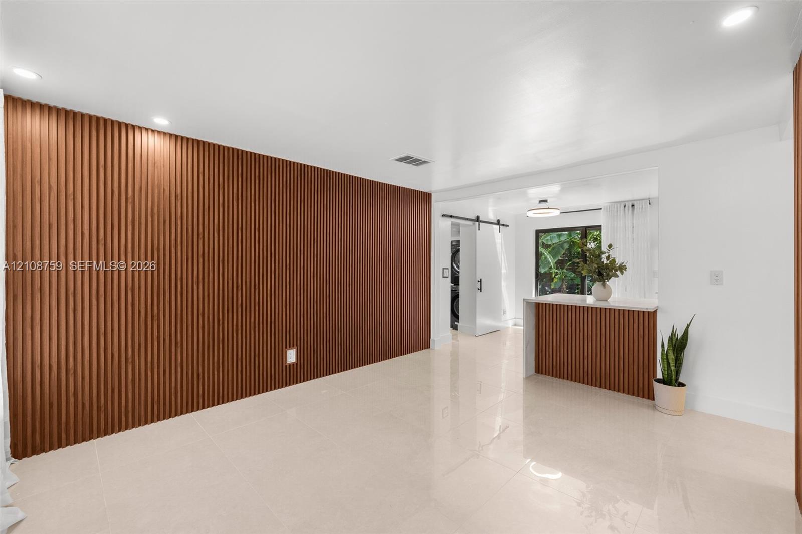 Large-format tile flooring, vertical wood-slat accent wall, built-in breakfast bar with matching wood-slat detailing, and a black metal barn door