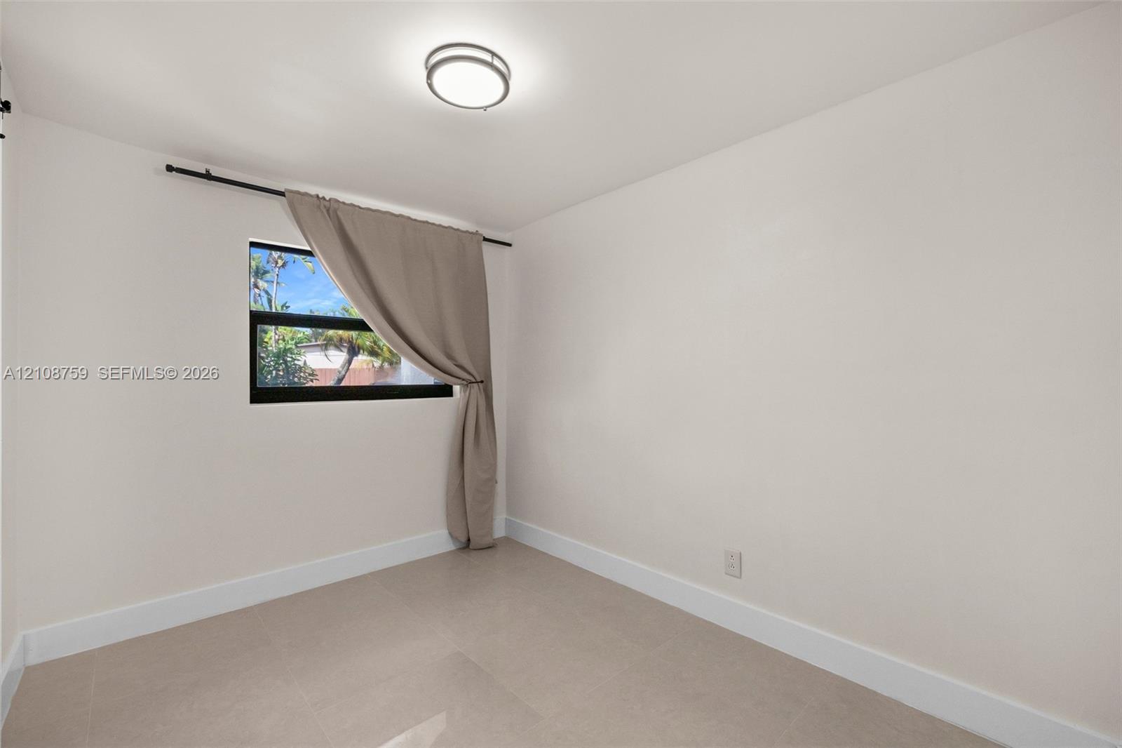 Neutral-toned ceramic tile flooring, clean wall finishes, and a dark-framed window featuring a mounted curtain rod and flush-mount overhead lighting